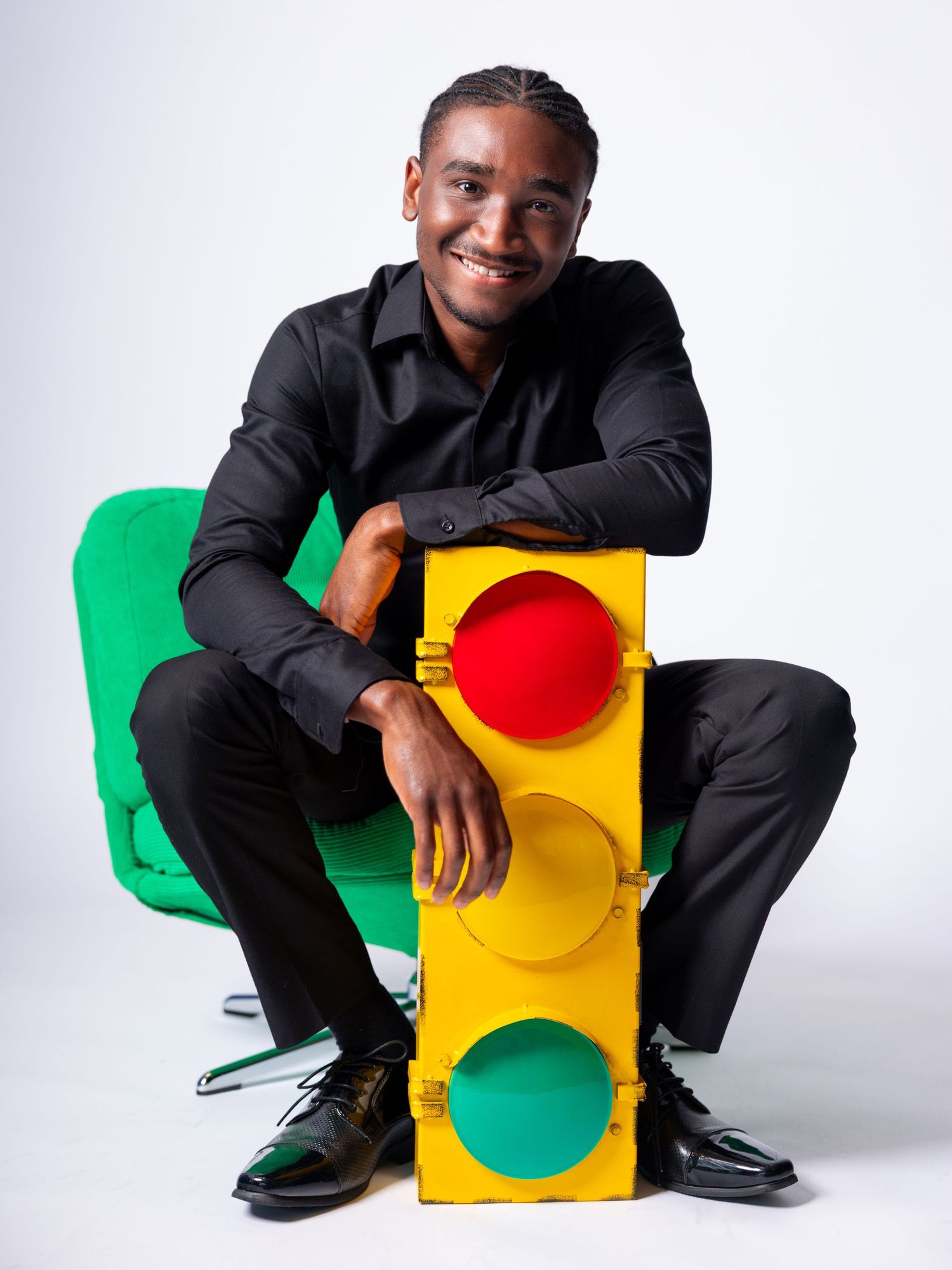 Smiling man in black outfit posing with a colorful traffic light prop on white background.