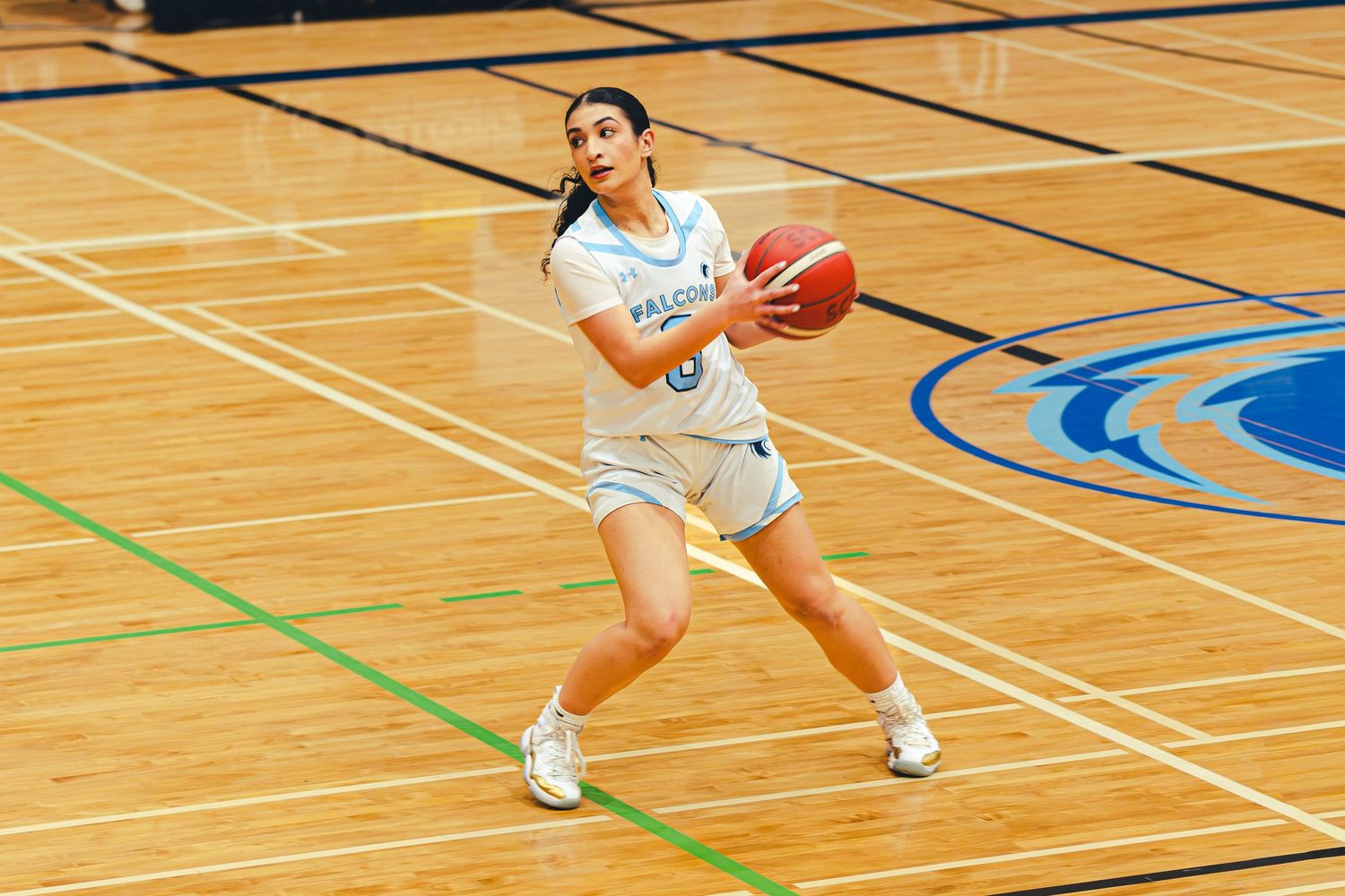 Female basketball player in white uniform prepares to pass ball on indoor hardwood court during a game.