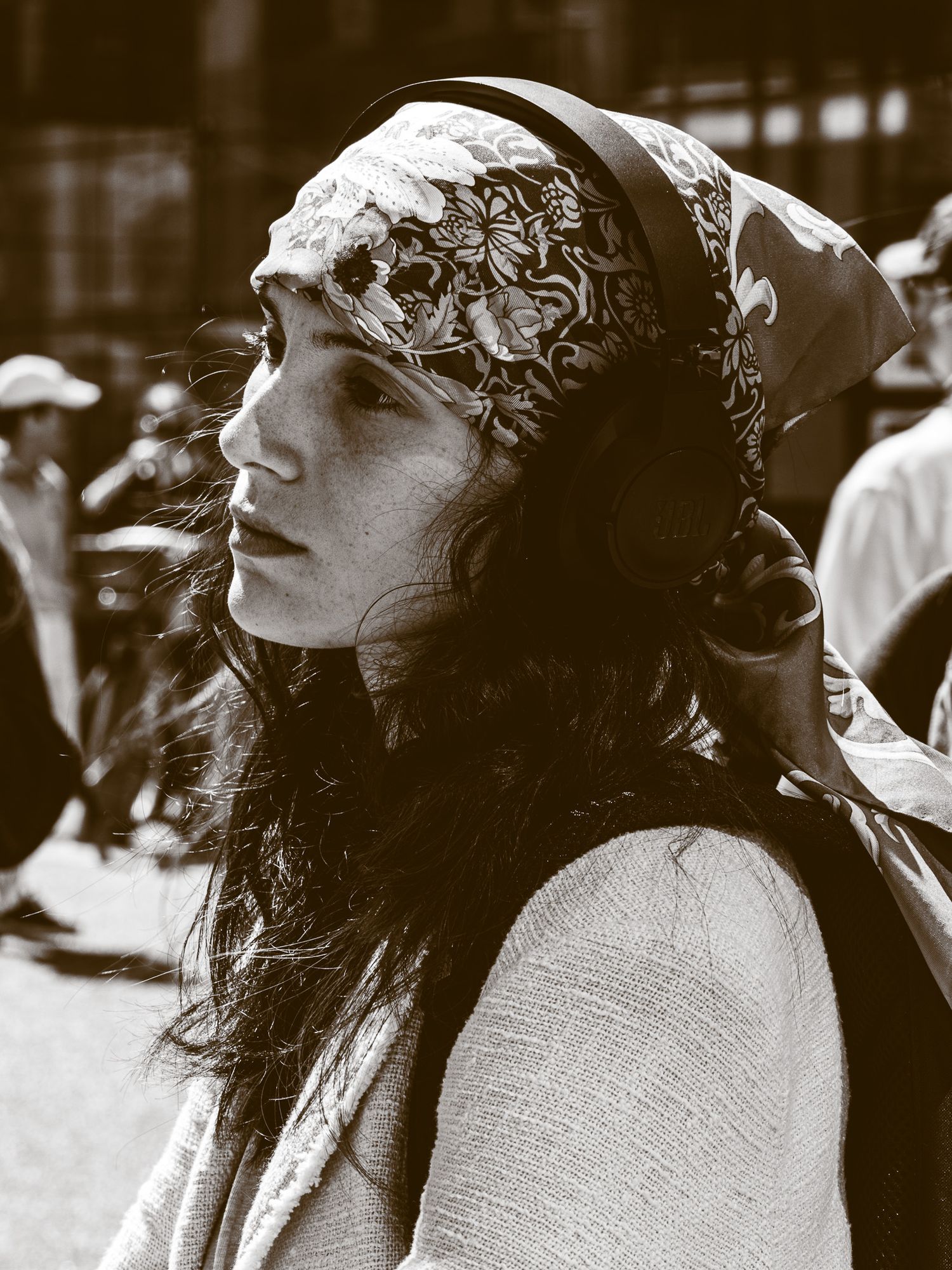 Black and white portrait of a woman wearing a patterned headscarf in an outdoor crowd.