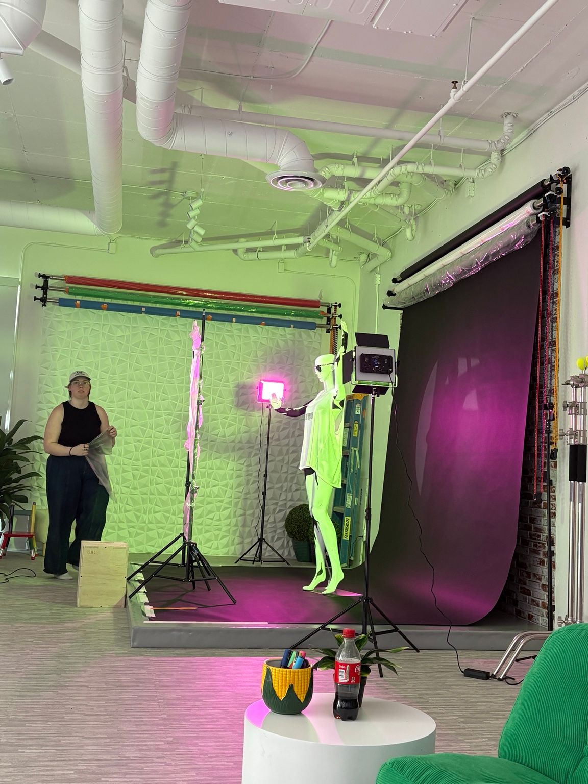 Photography studio with green screen, purple backdrop, mannequin, pink LED light, and person standing nearby.