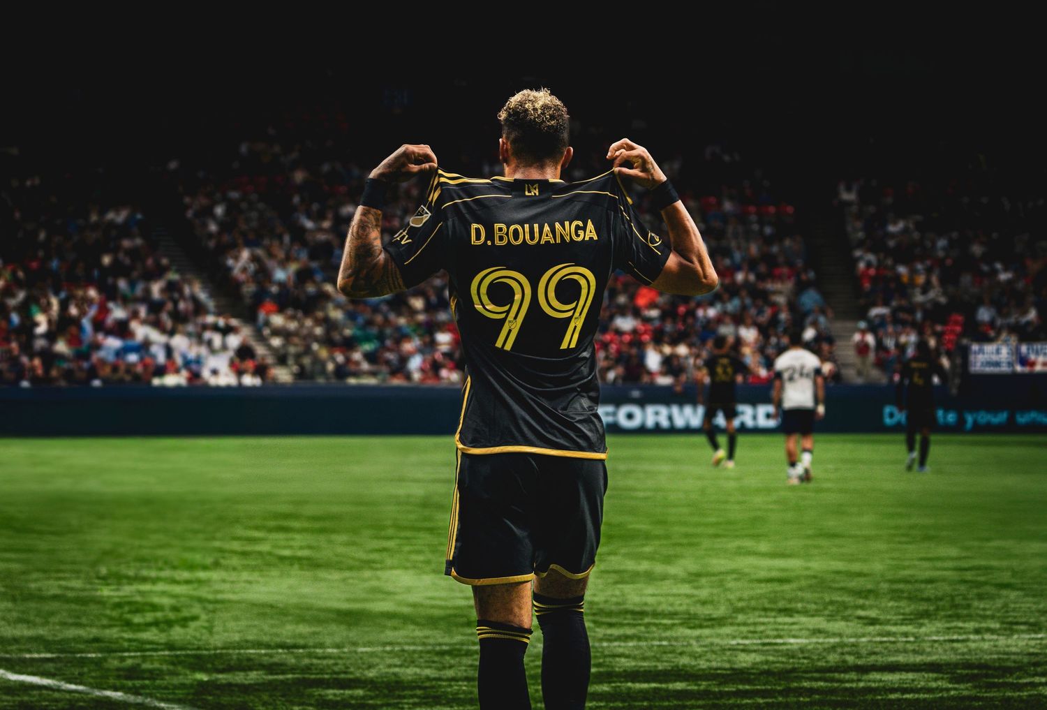 Soccer player number 99 D. Bouanga holding up his jersey to the crowd in a dark stadium.
