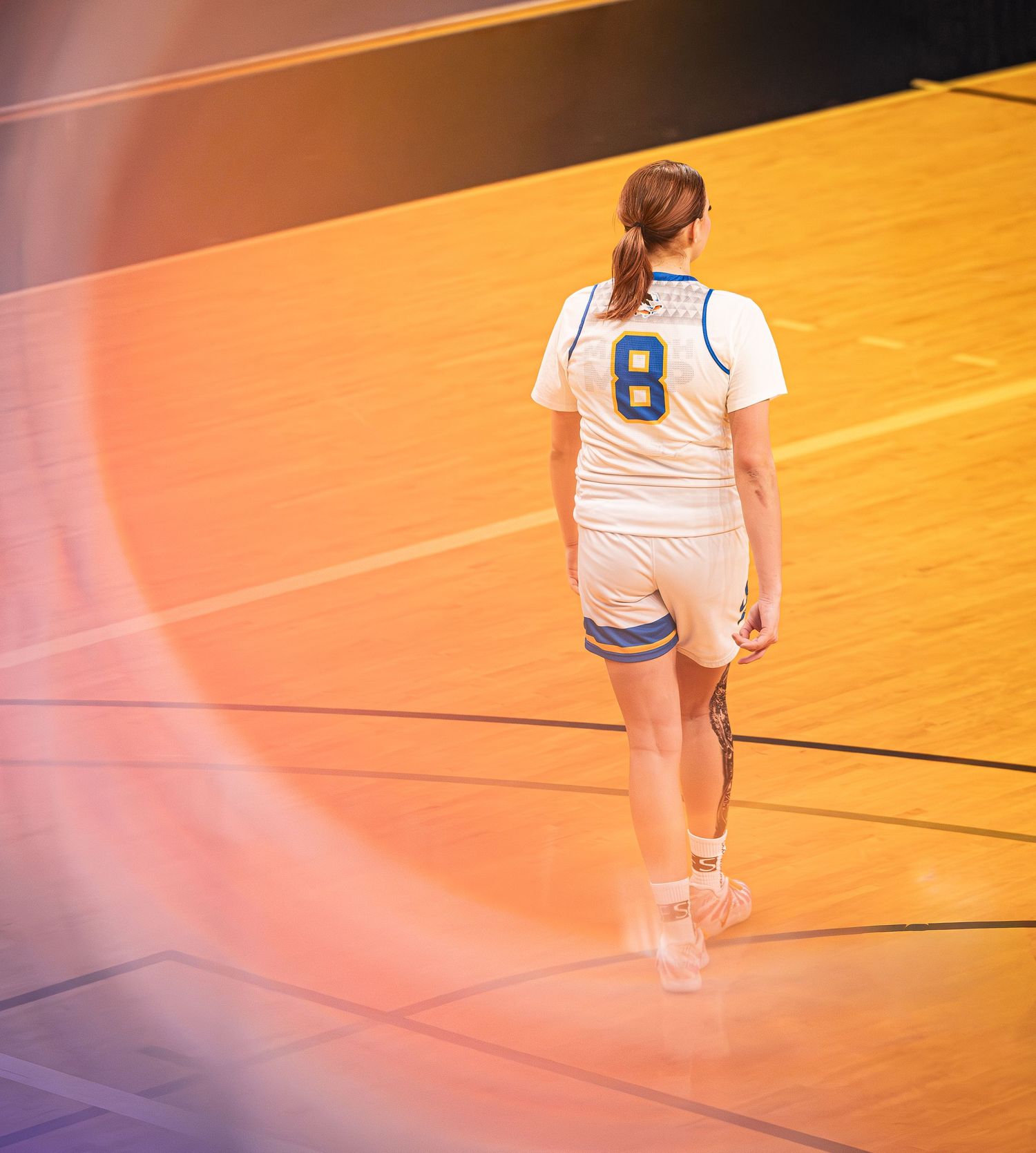 Female basketball player wearing number 8 white and blue uniform walking on an indoor court.