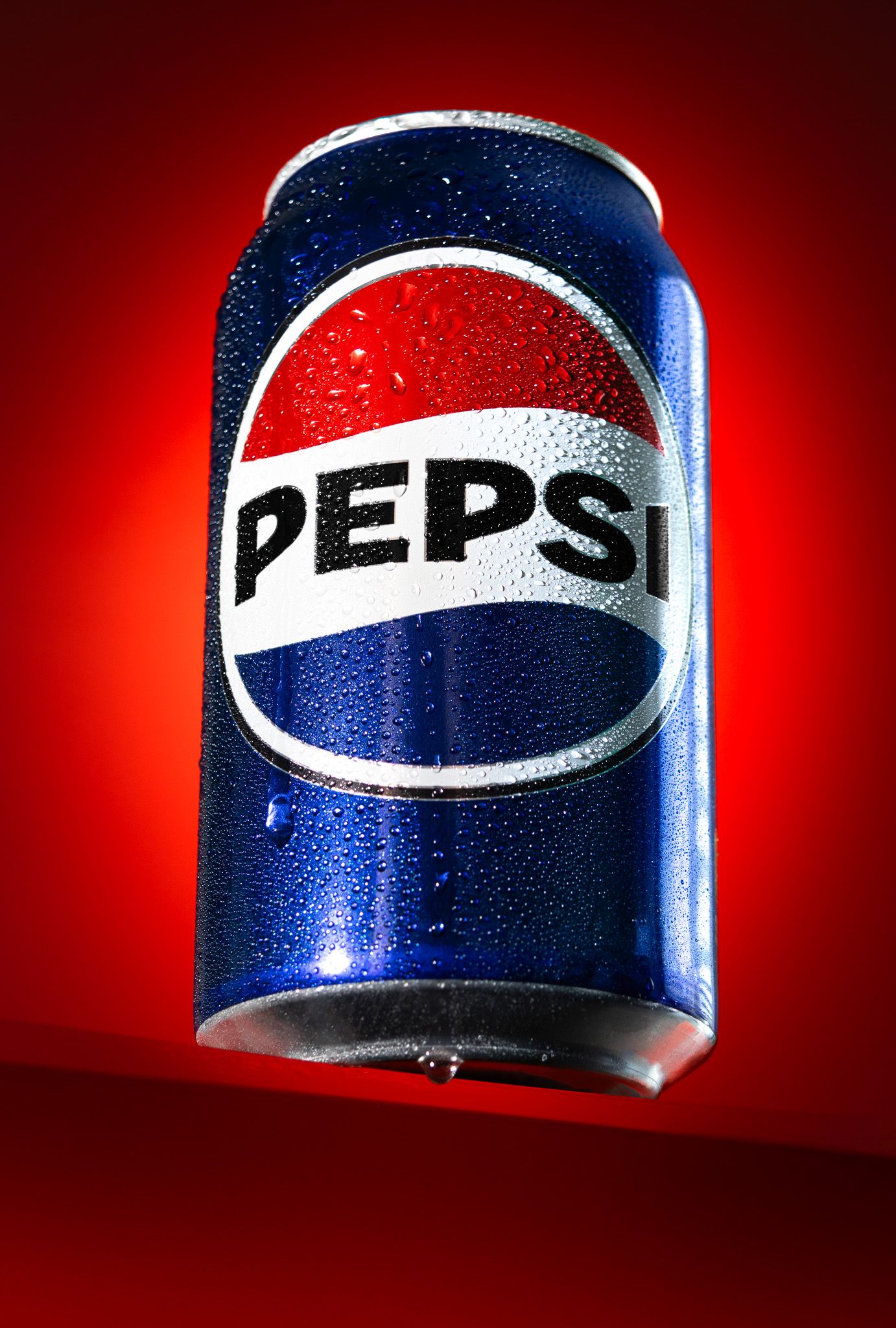 Pepsi cola can covered in water droplets floating against a bold red background.