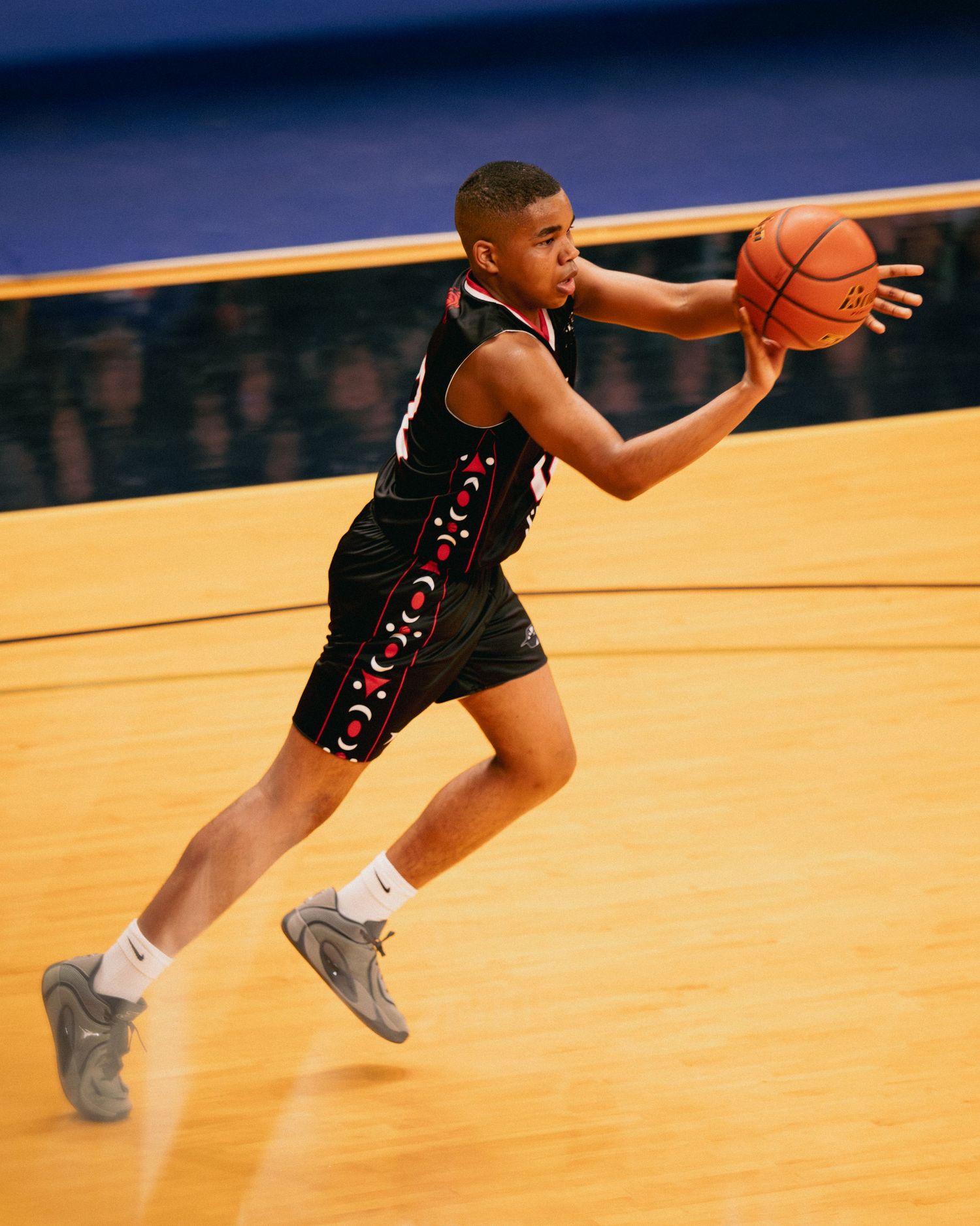 Young male basketball player in black uniform dribbling ball on an indoor court.
