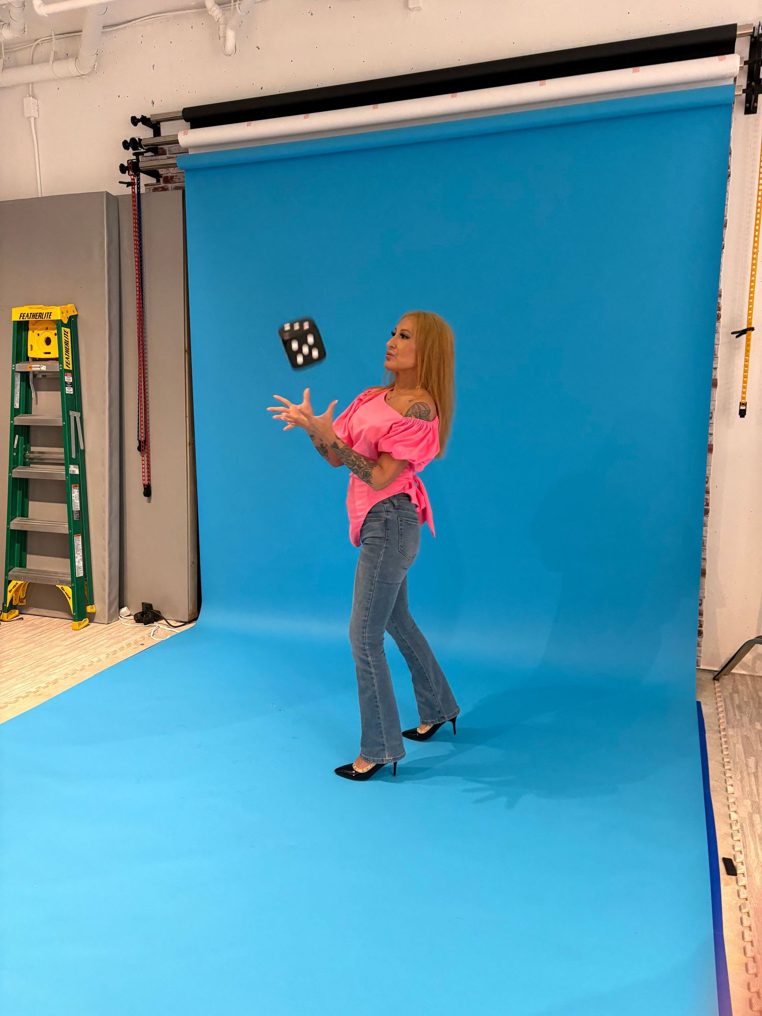 Woman in pink top and jeans tossing an object in a professional photography studio with blue backdrop.