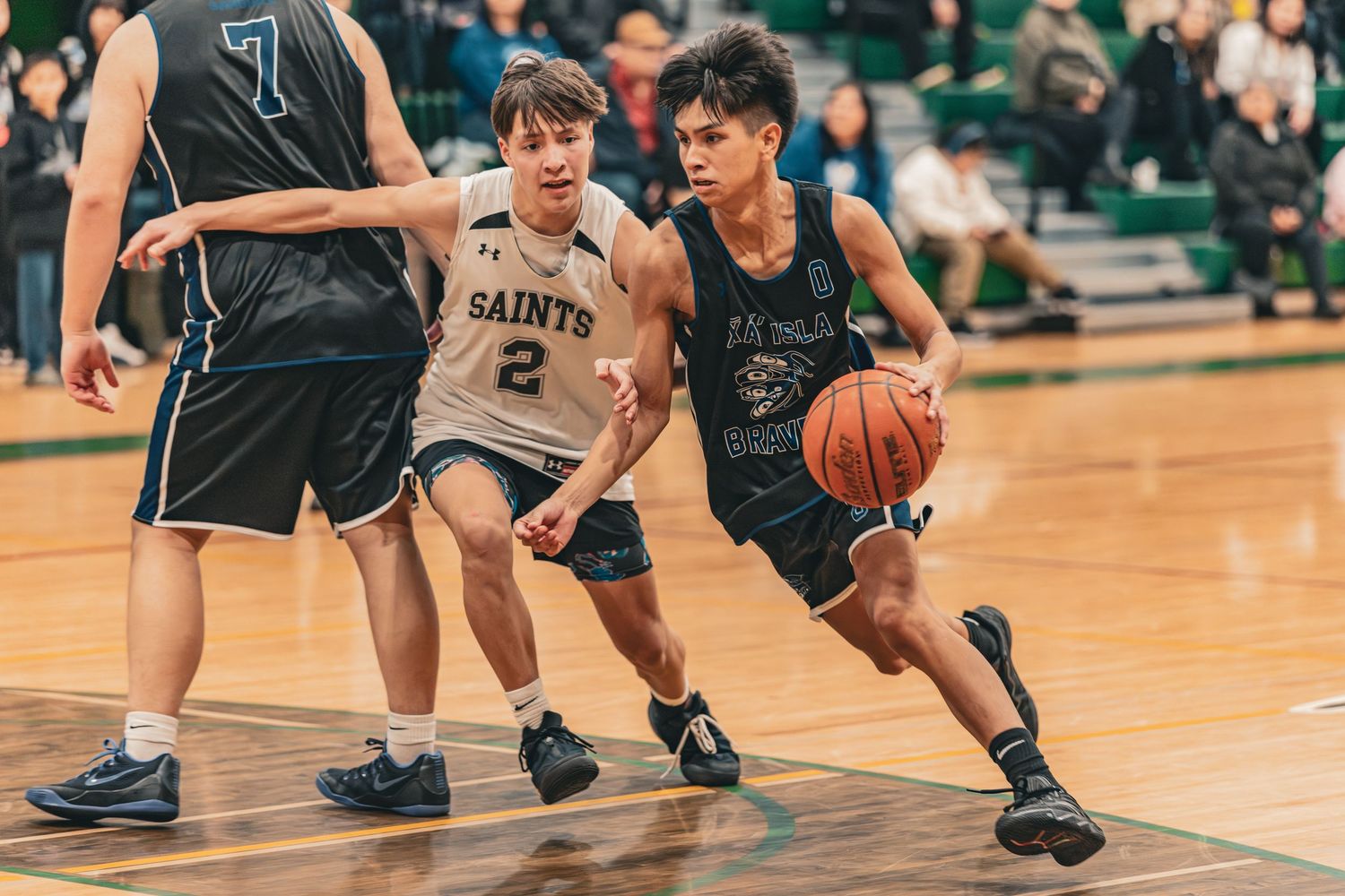 Basketball player in dark uniform drives past Saints defender number 2 during game.