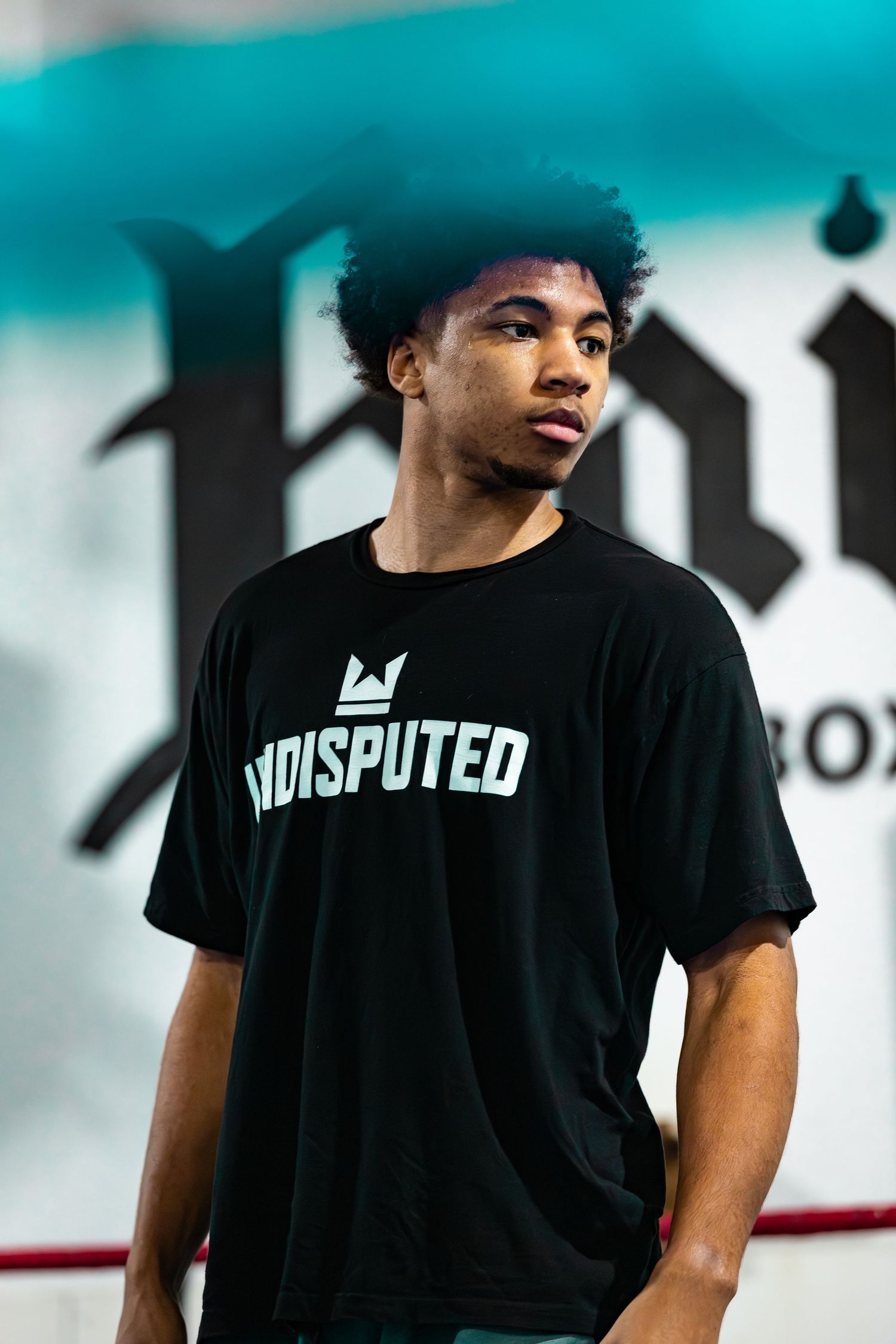 Young man wearing a black Undisputed t-shirt standing in a boxing gym.