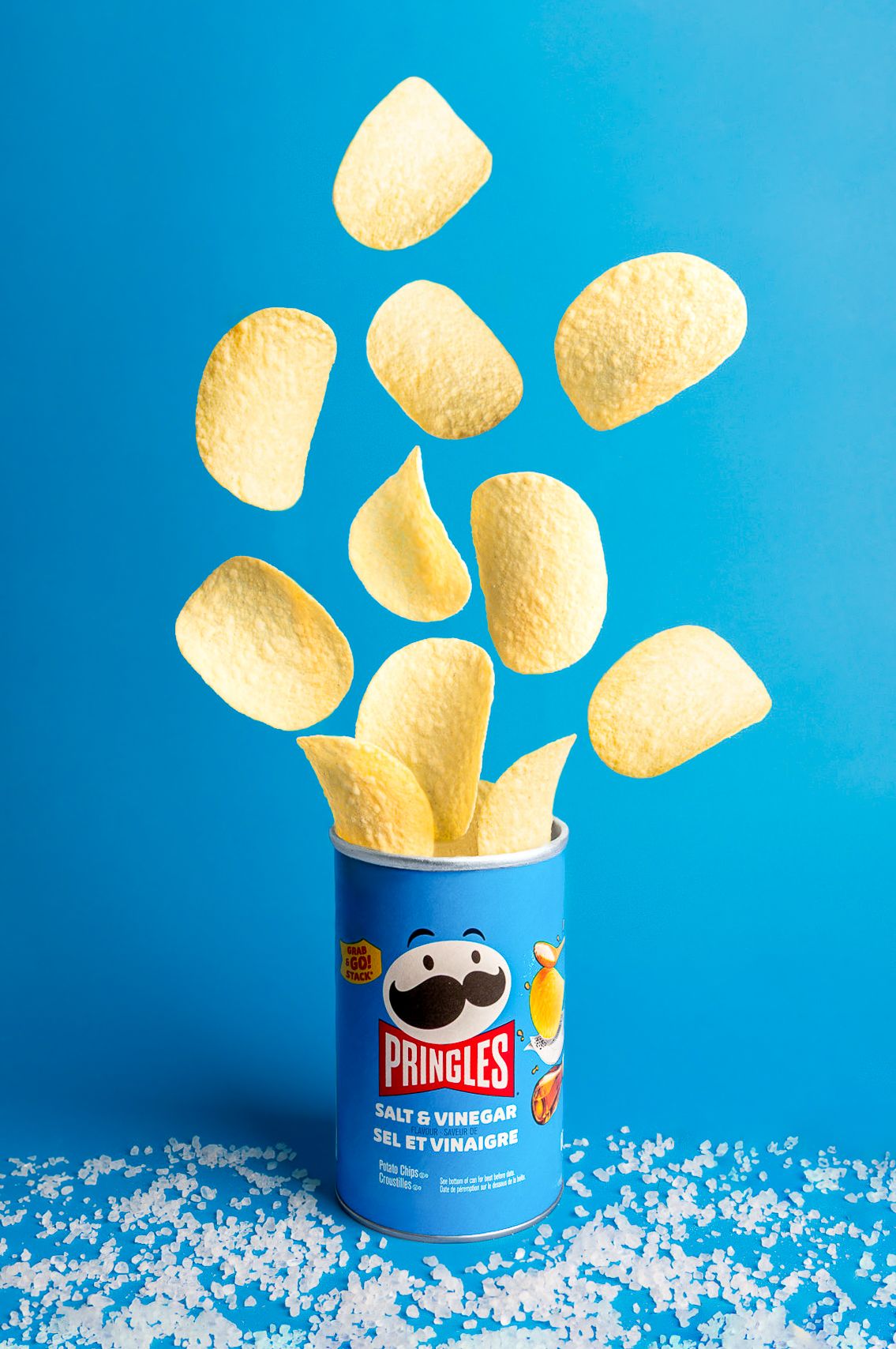Pringles Salt and Vinegar chips flying out of blue canister on bright blue background.