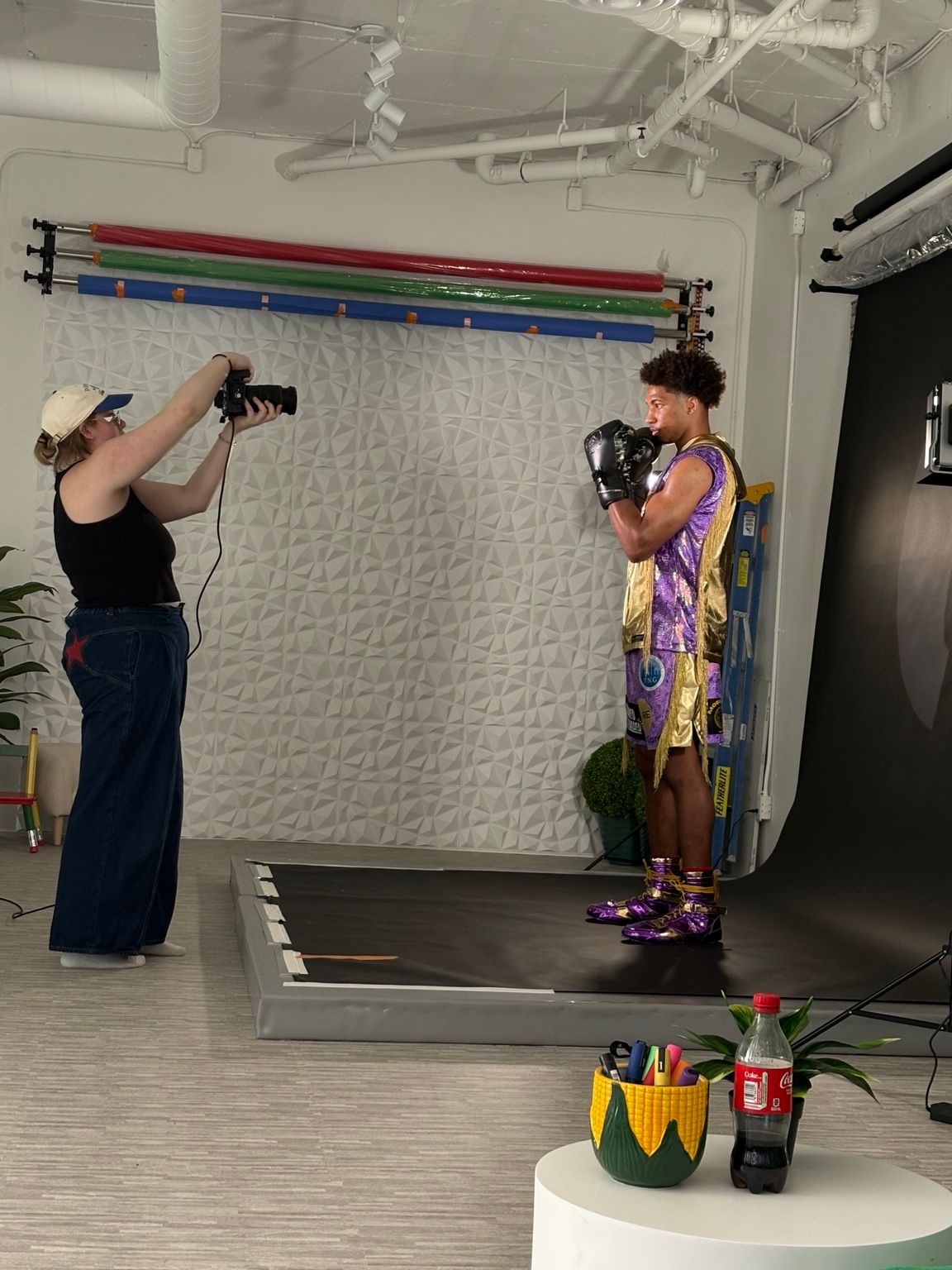 Photographer capturing a male model in boxing gloves and purple outfit against white backdrop in professional studio.