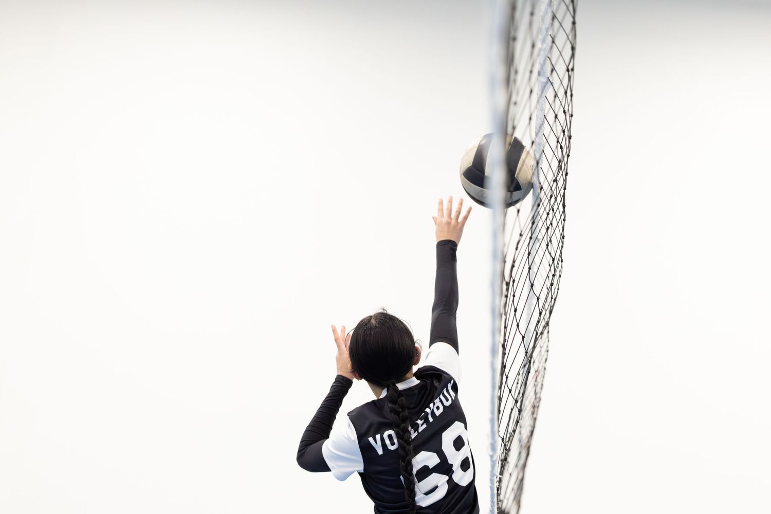 Volleyball player number 68 reaching to block ball at net during game.