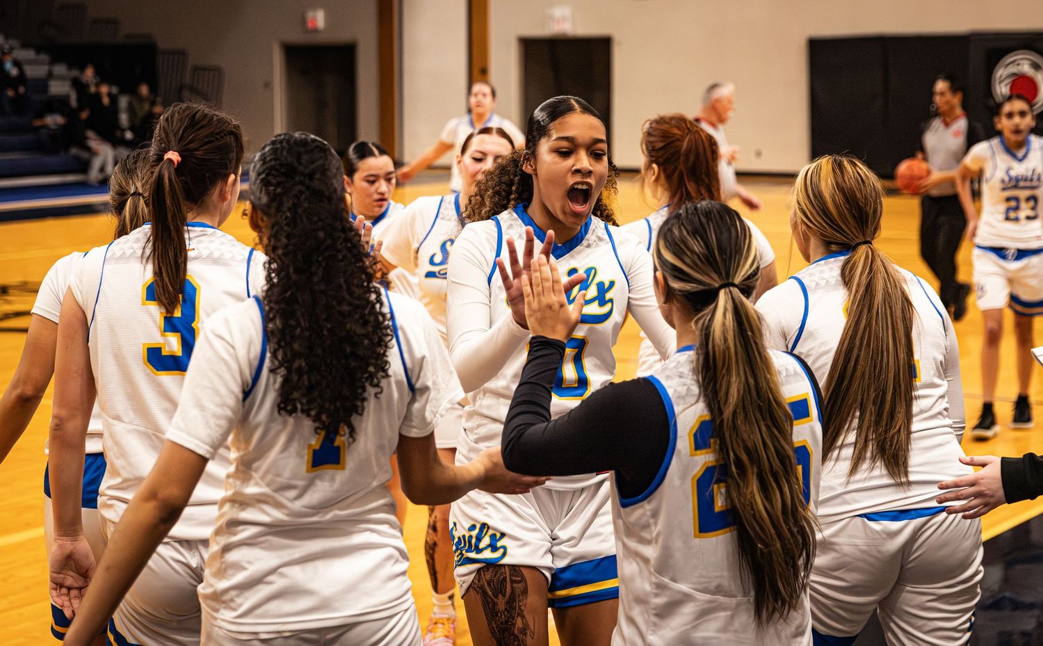 Female basketball team in white Suits uniforms celebrating together on an indoor court.