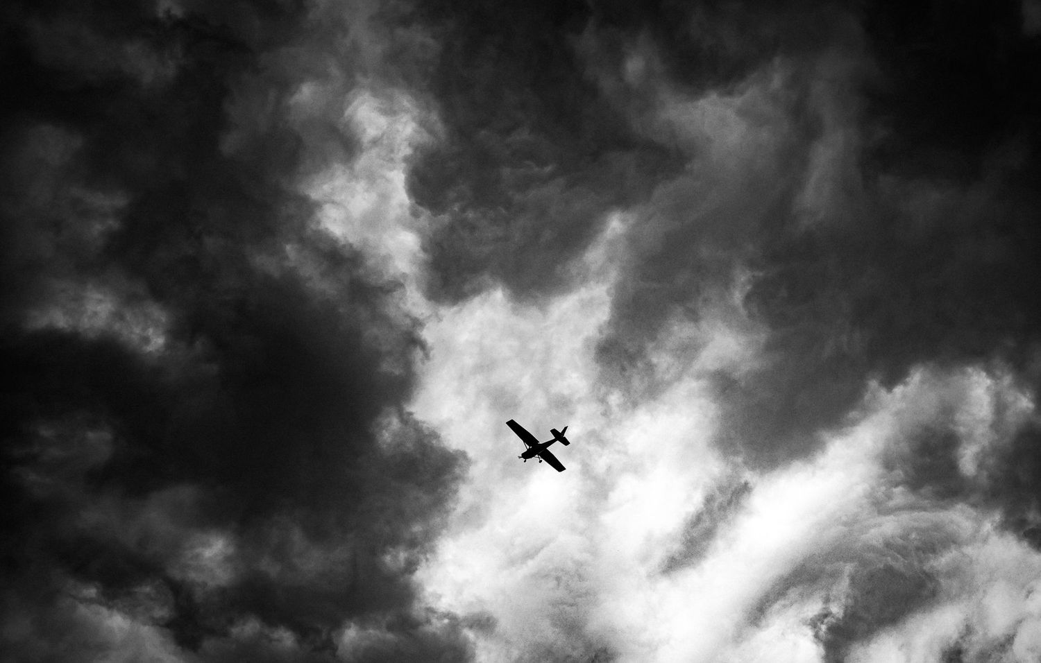 Black and white photo of a small airplane silhouetted against dramatic stormy clouds in the sky.