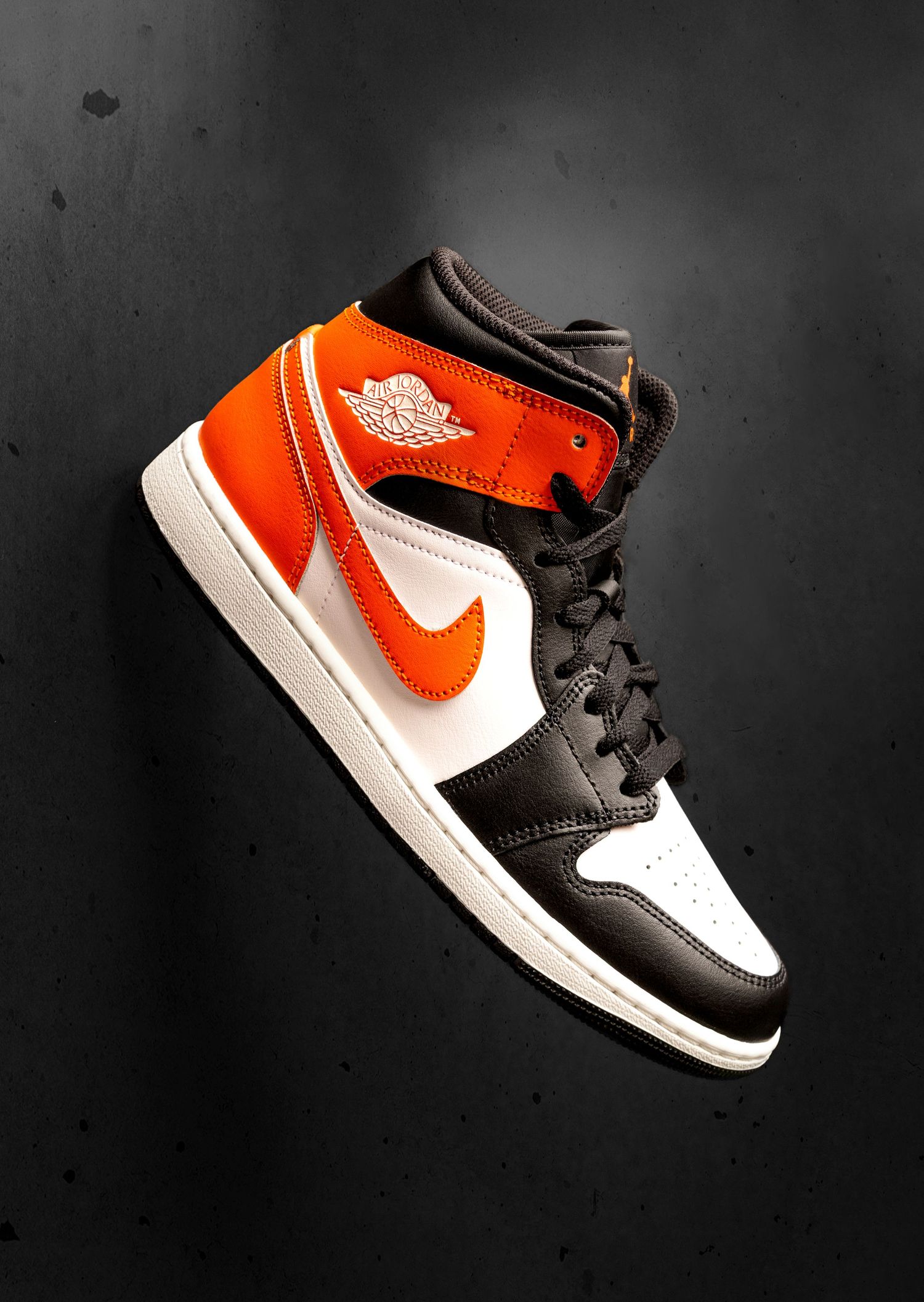 Air Jordan 1 Retro High OG sneaker in black, white, and orange colorway floating on dark background.