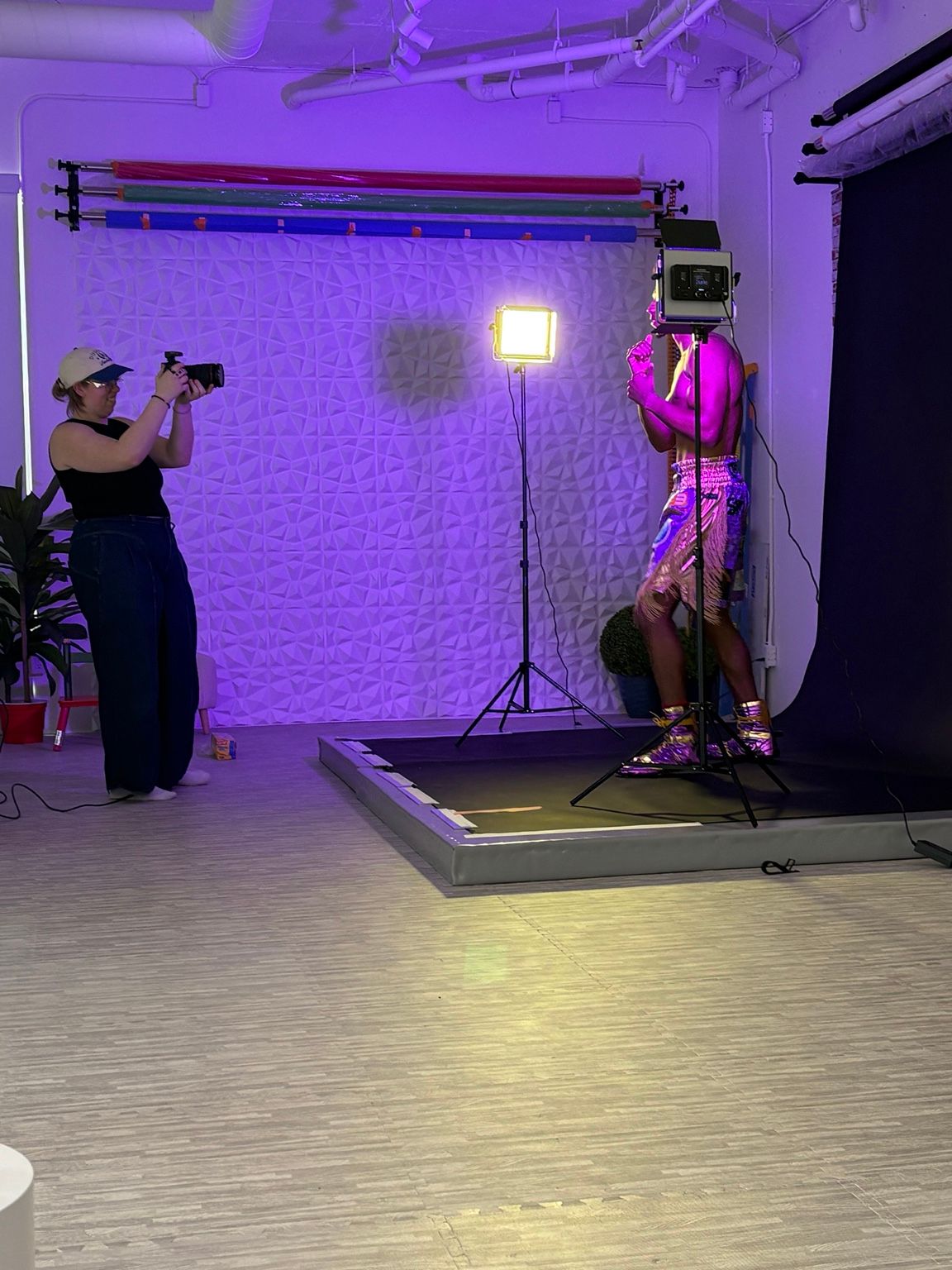 Photographer capturing a model in a pink outfit under studio lights with colorful backdrop rolls in a white studio.