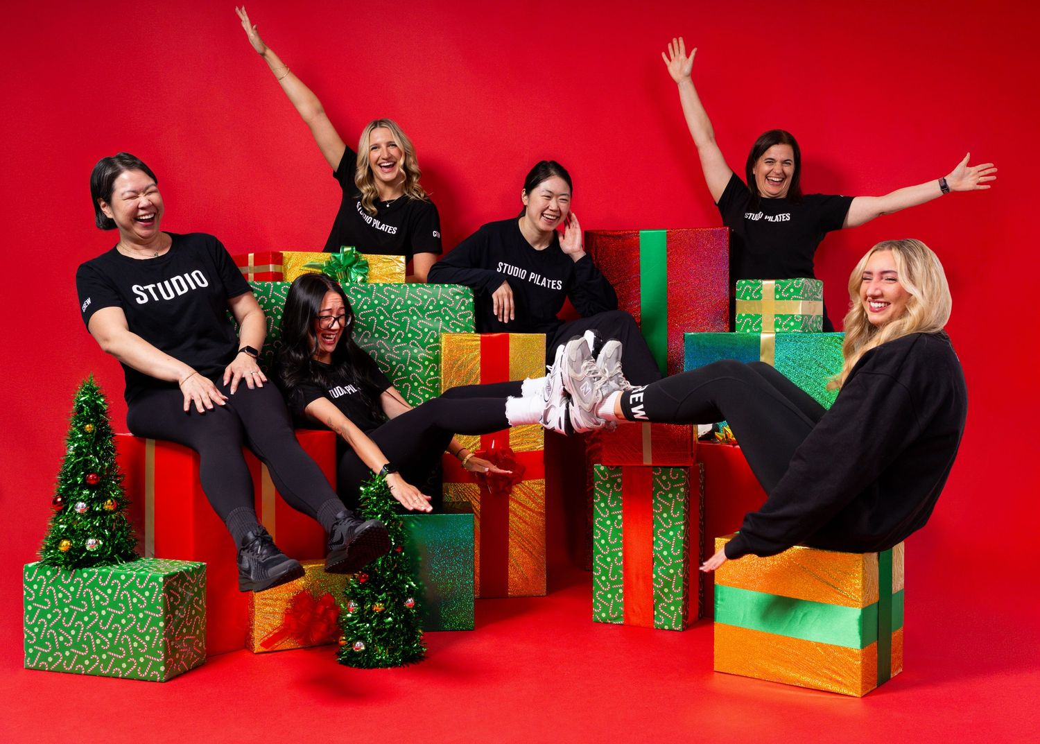 Group of six people in black Studio shirts celebrating Christmas with colorful gift boxes on a red background.