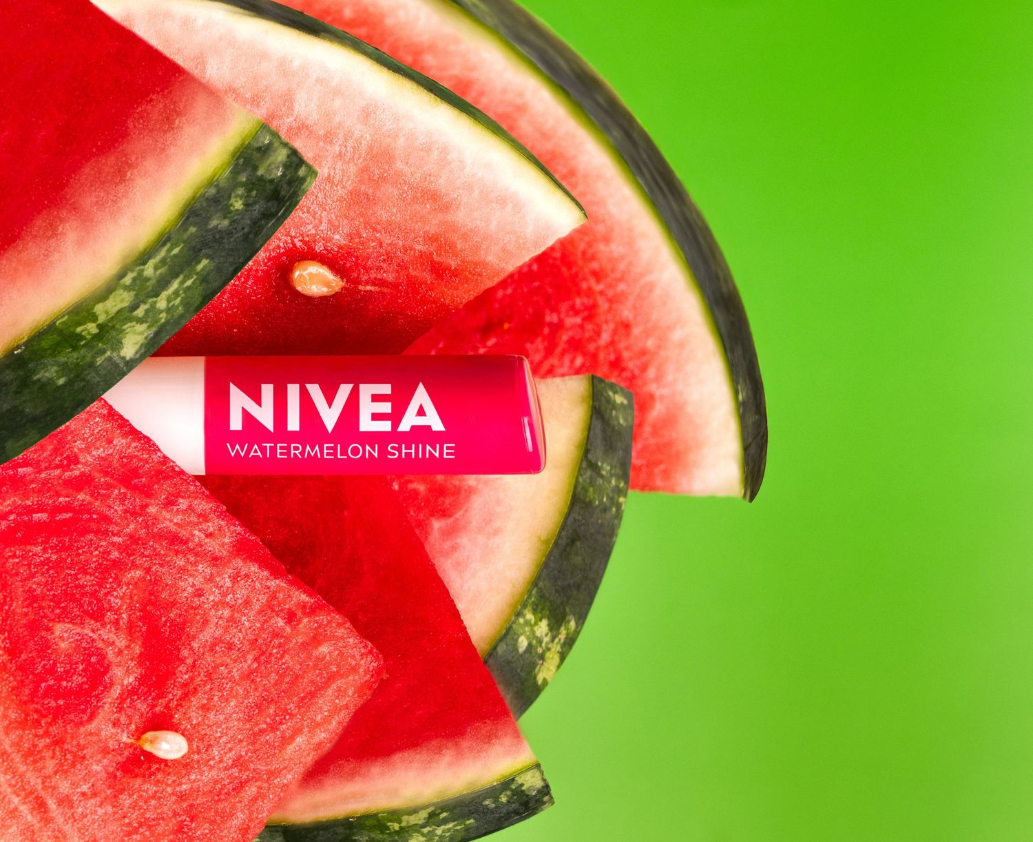 Nivea Watermelon Shine lip balm surrounded by fresh watermelon slices on green background.
