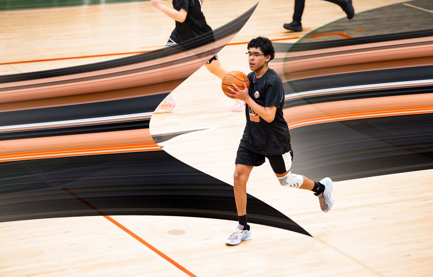 Young male basketball player dribbling on court during warmup practice session.