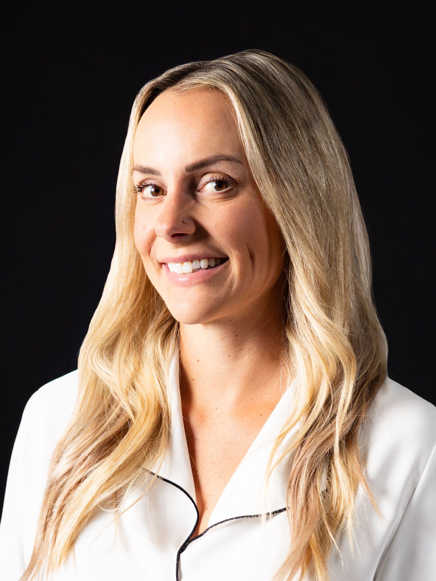 Professional headshot of a smiling blonde woman in a white blazer against a dark background.
