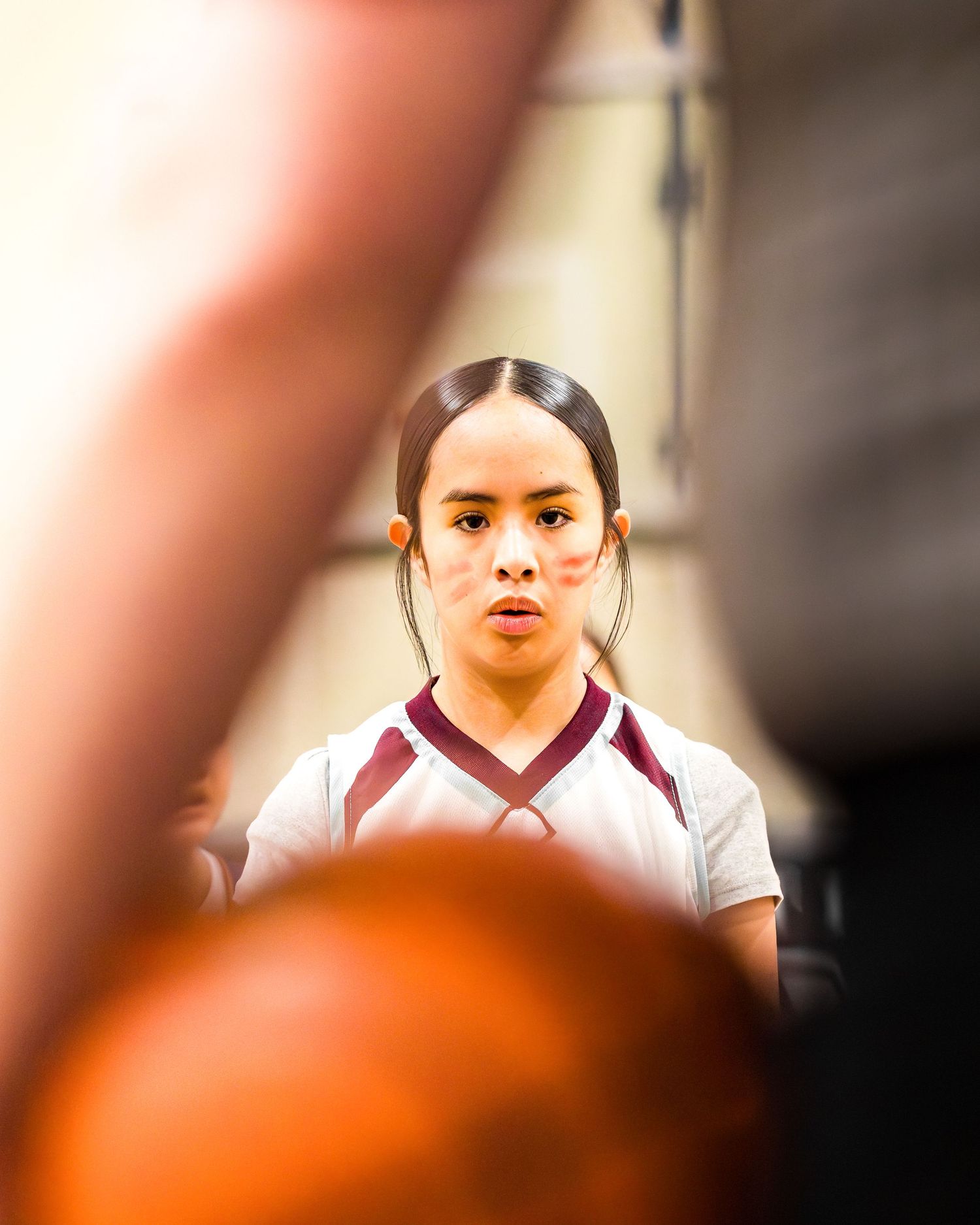 Young female basketball player in maroon uniform focused during a game timeout huddle.