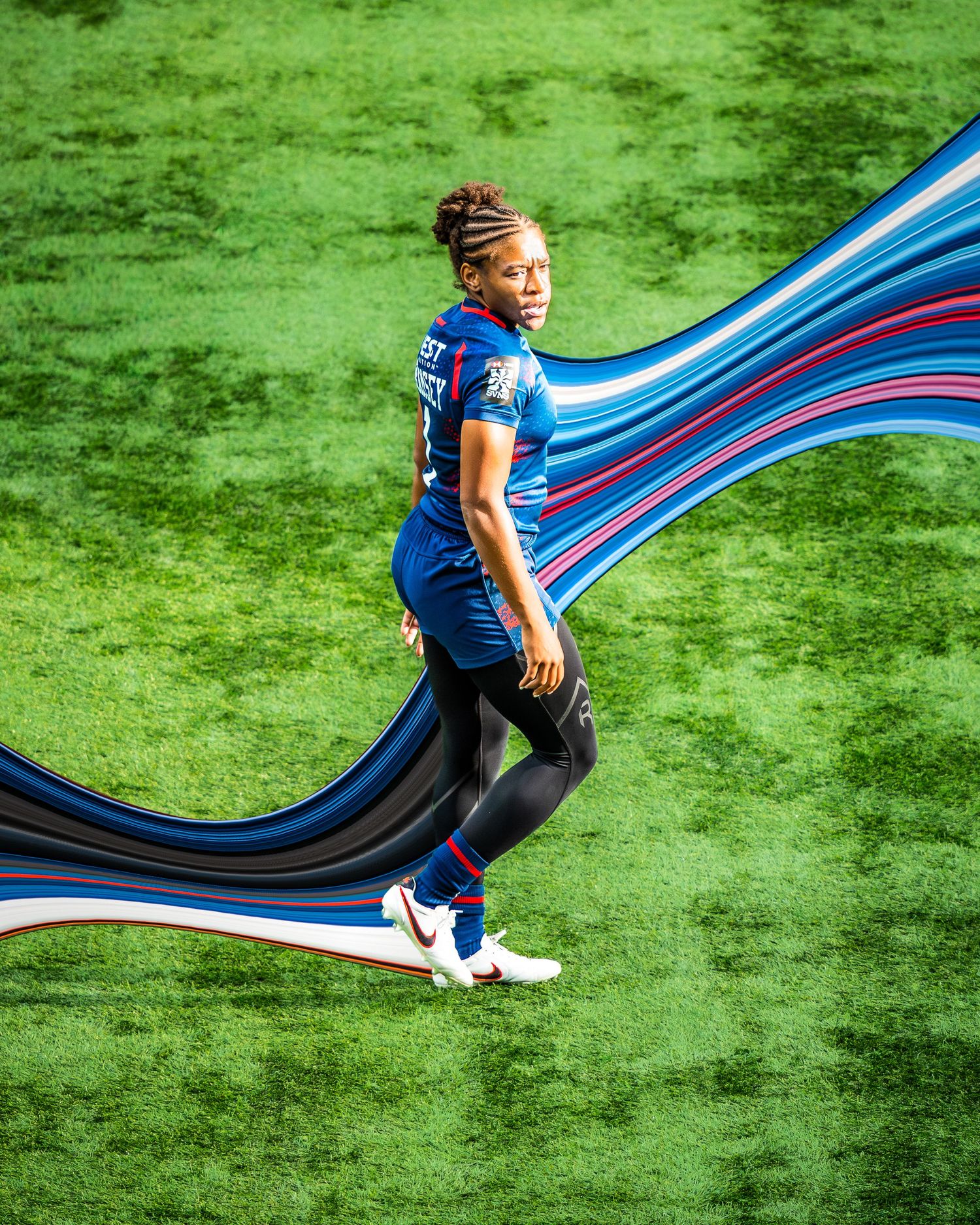 Female soccer player in blue jersey posing with flowing ribbon on field.
