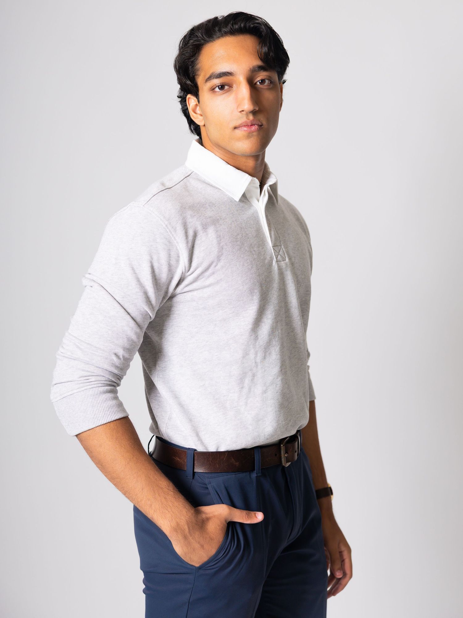 Man wearing a light gray long-sleeve polo shirt with white collar, paired with navy trousers and brown belt.