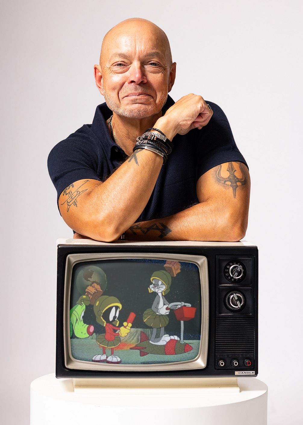 Bald tattooed man posing with a vintage CRT TV displaying Looney Tunes cartoon characters on white background.