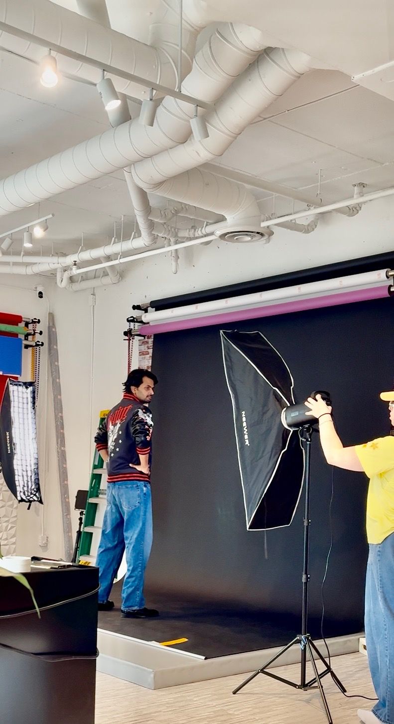 Two photographers set up a professional studio with a black backdrop and softbox lighting equipment in a bright indoor space.