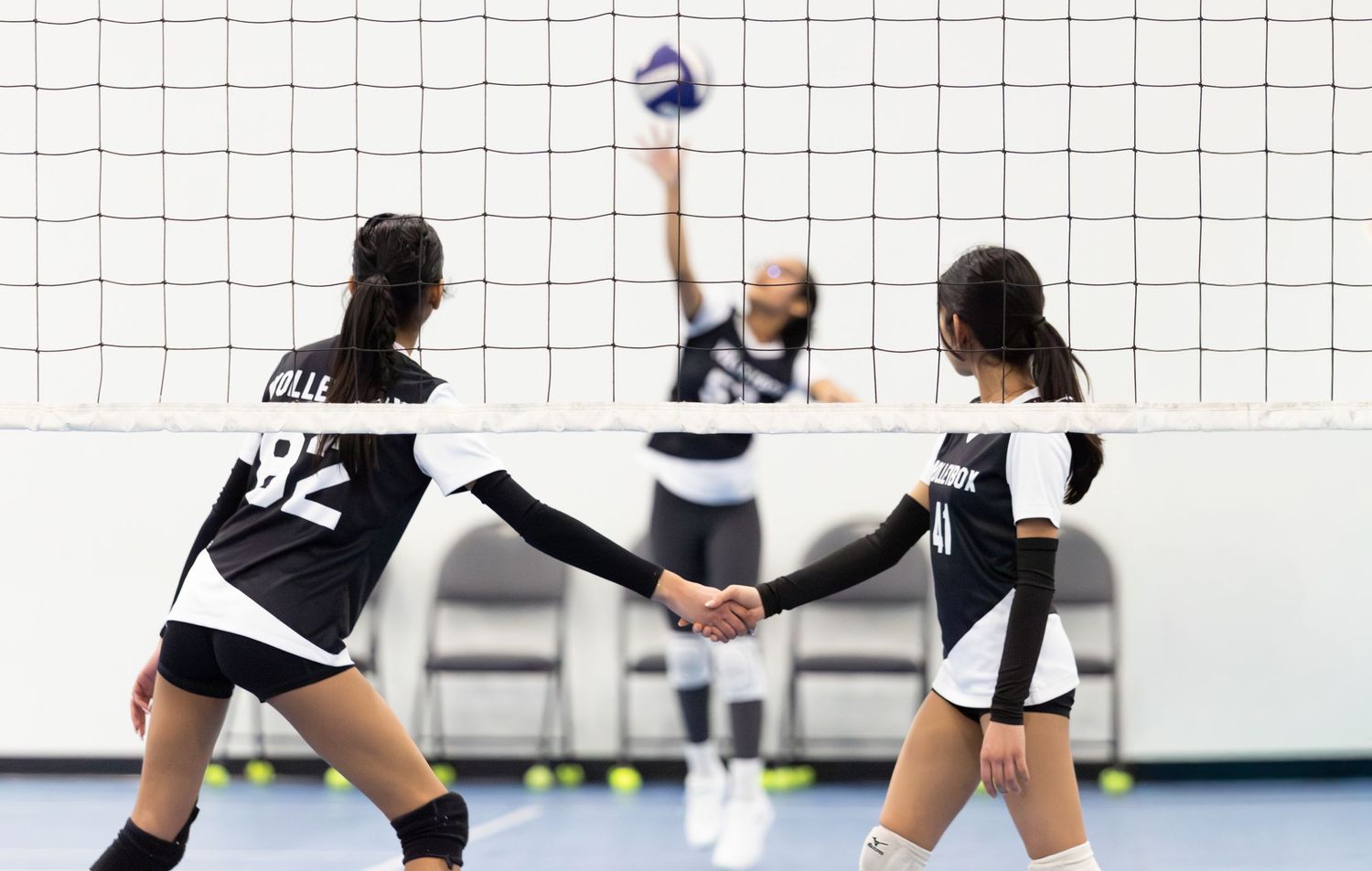 Two volleyball players in black uniforms shaking hands near net during match.