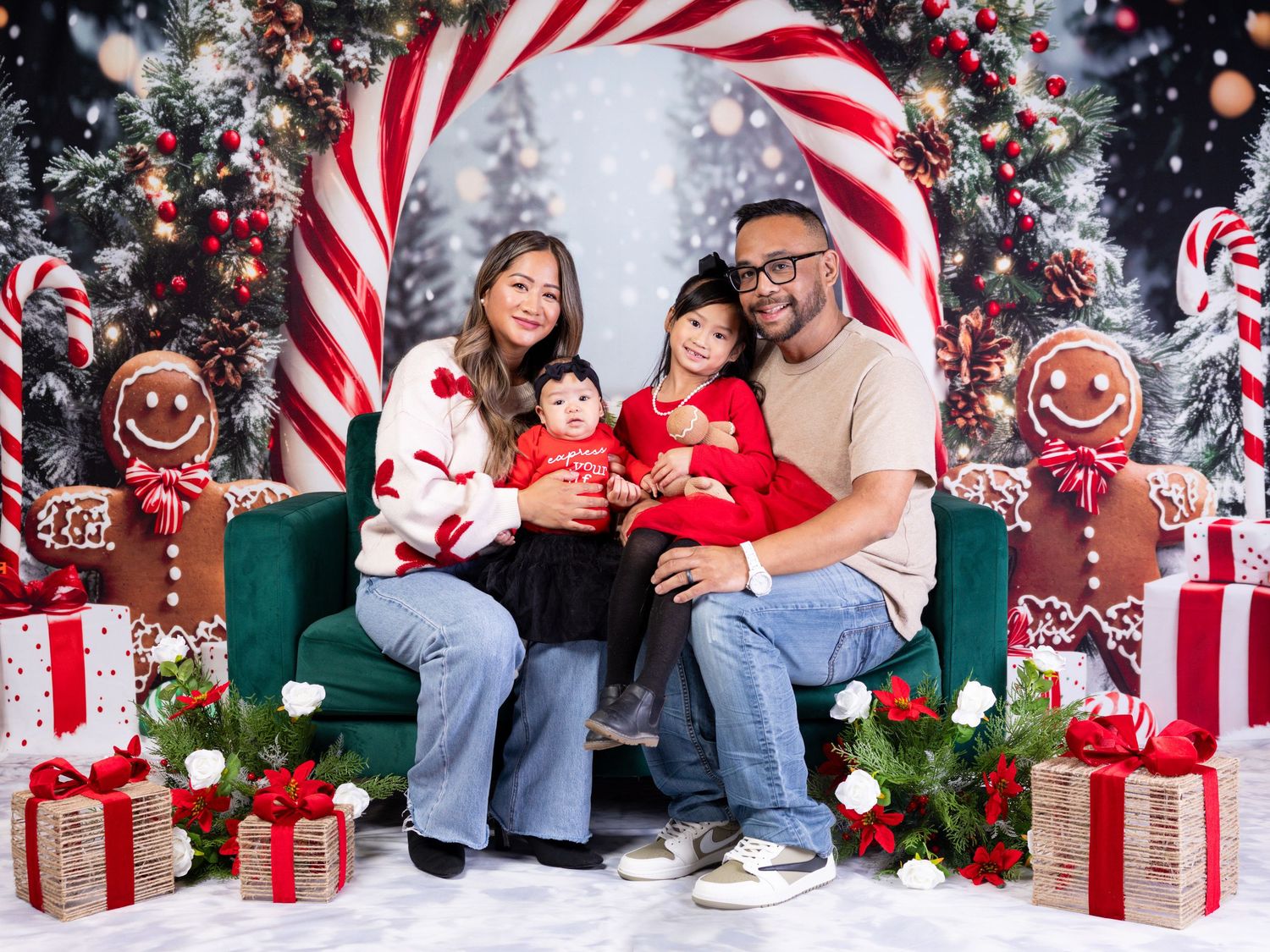 Family of four posing for a festive Christmas photo with candy canes, gingerbread, and holiday gifts backdrop.