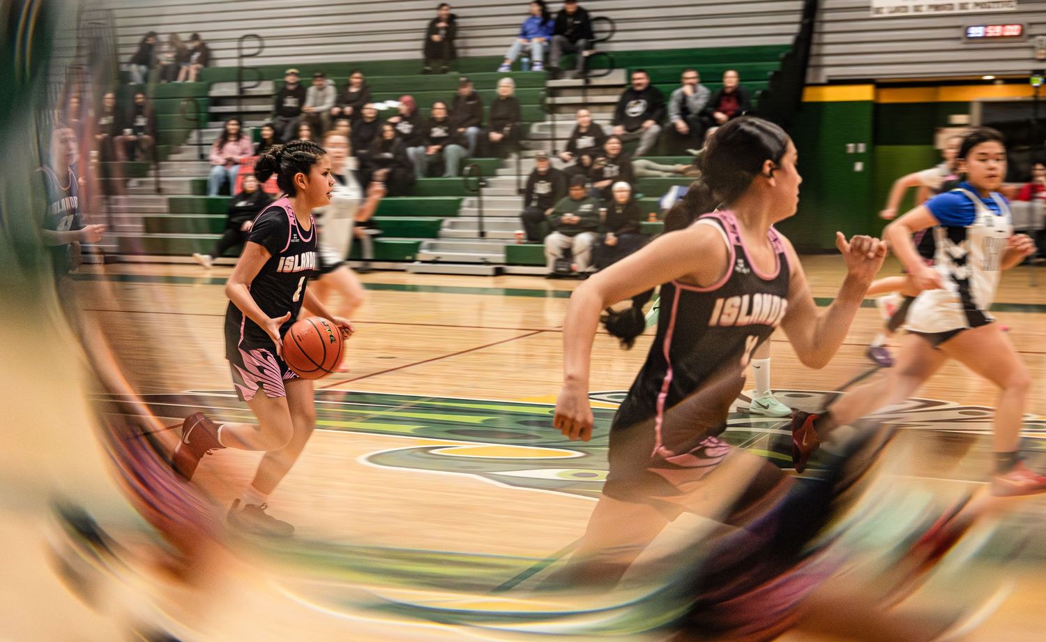 Female basketball players in black uniforms running on court captured with motion blur effect.