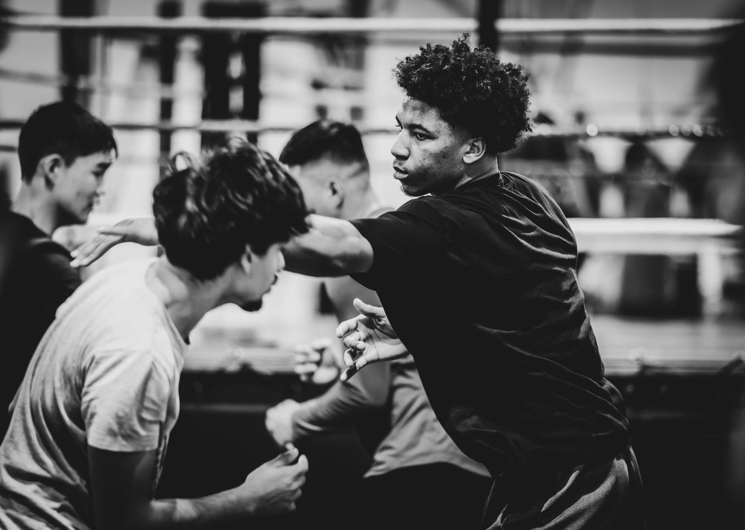 Two young male boxers sparring in a gym, one throwing a punch while the other defends in black and white.