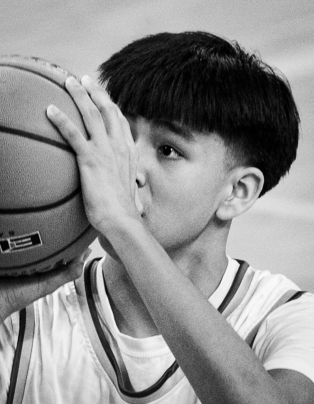 Young male basketball player holding ball up to face in black and white photo.