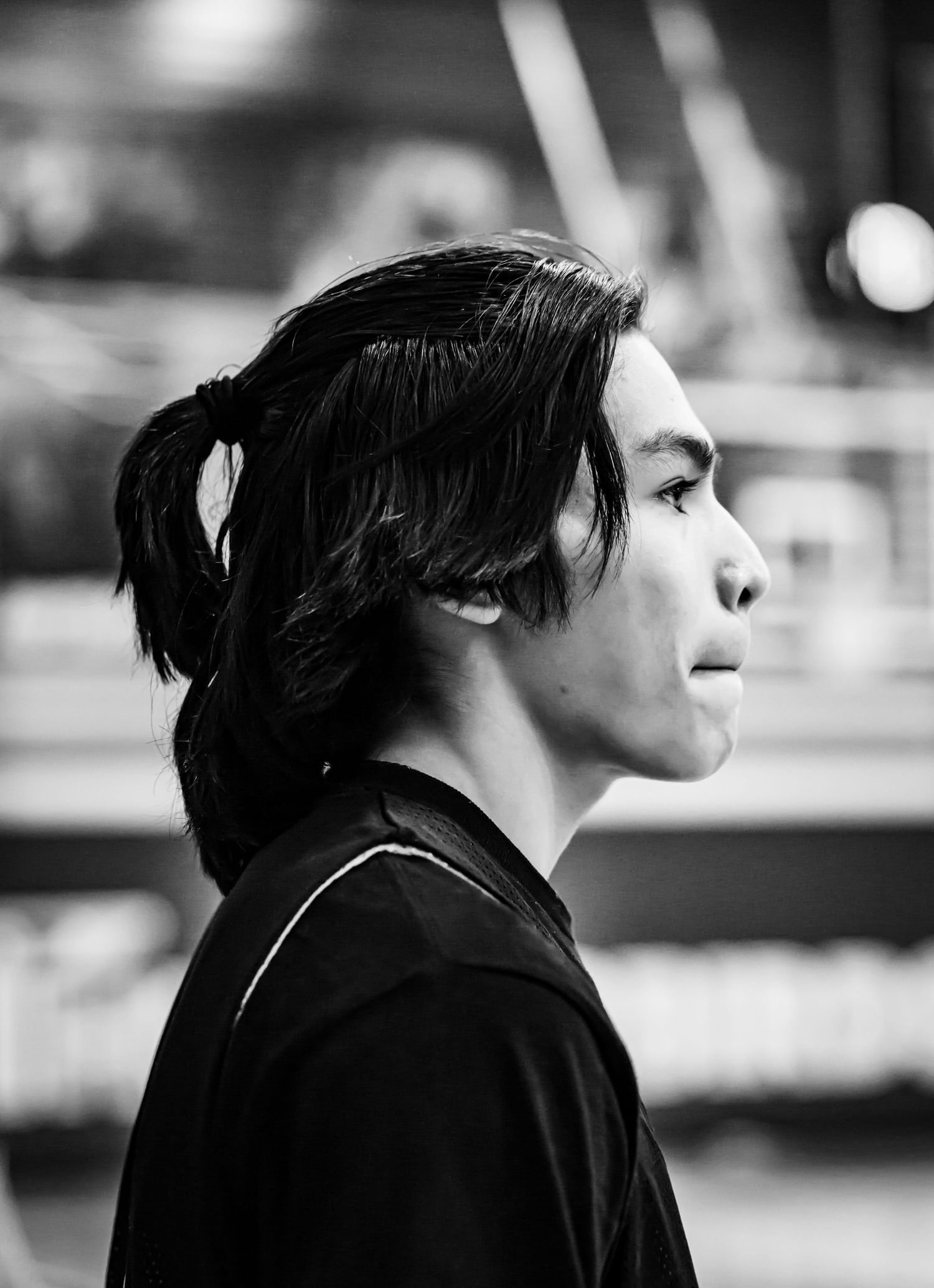 Black and white profile portrait of young male athlete with ponytail in gym.