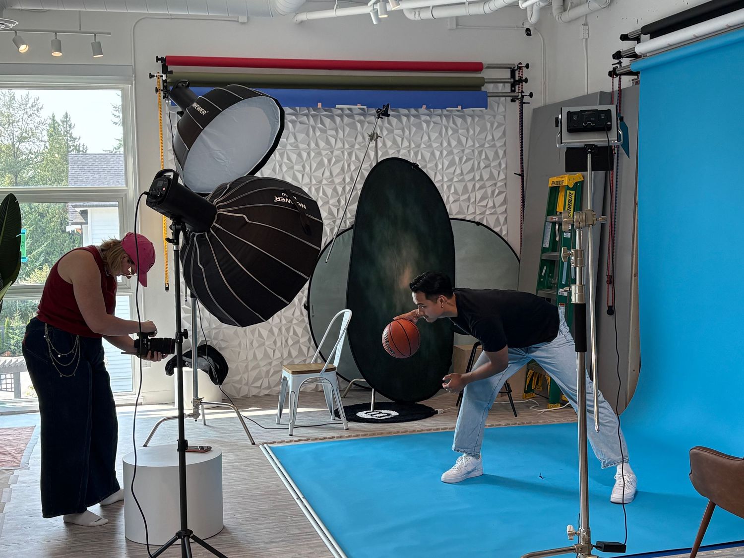 Two photographers work in a professional studio with softbox lights, colorful backdrops, and blue flooring during a photo shoot.