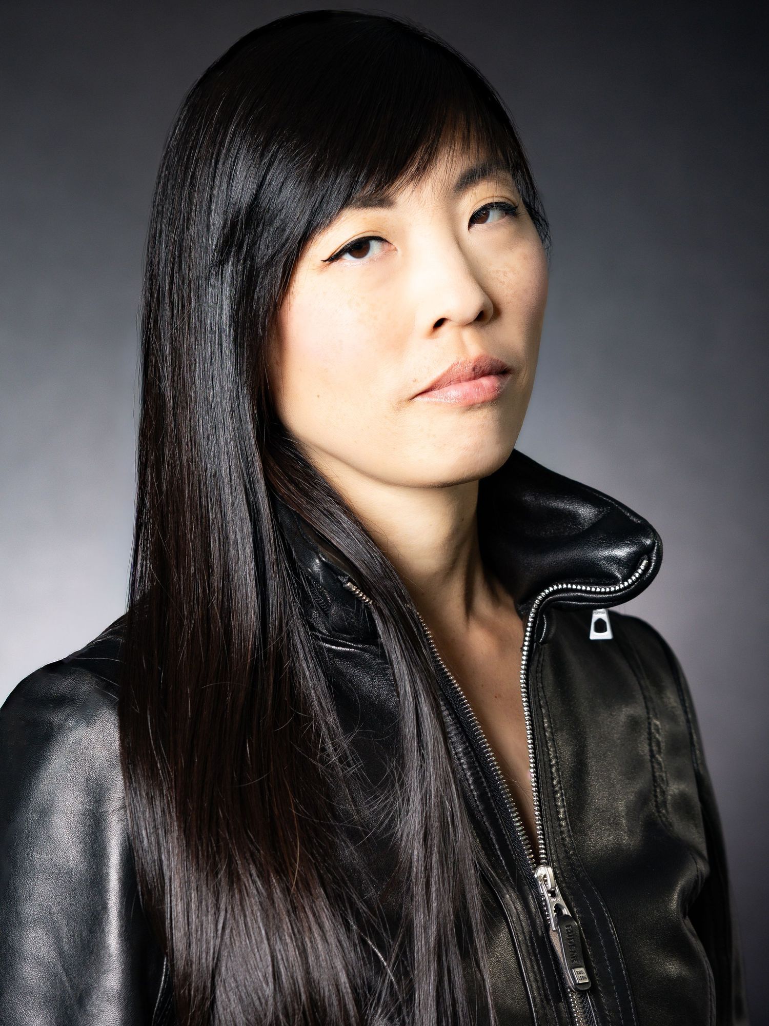 Young Asian woman with long black hair wearing a black leather jacket, posing for a professional portrait photo.