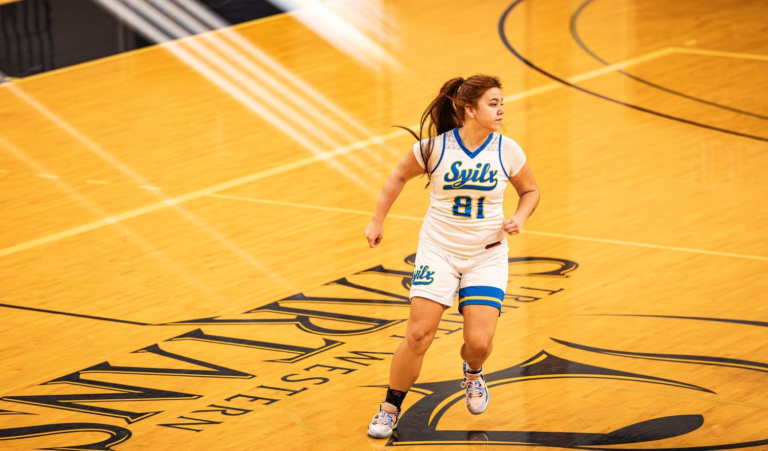Female basketball player in white Suits jersey number 81 running on a yellow court.