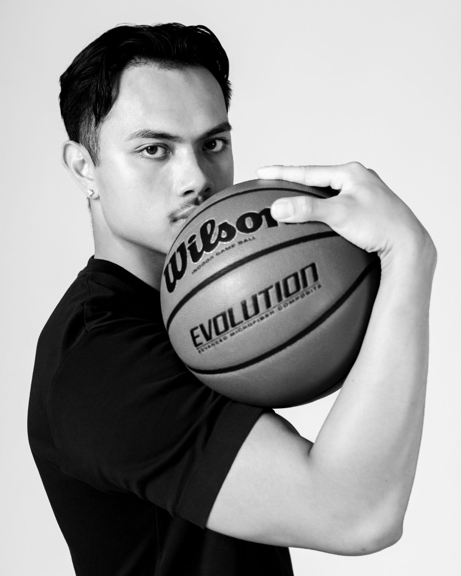 Black and white photo of a young man holding a Wilson Evolution basketball up to his face, wearing a black t-shirt.