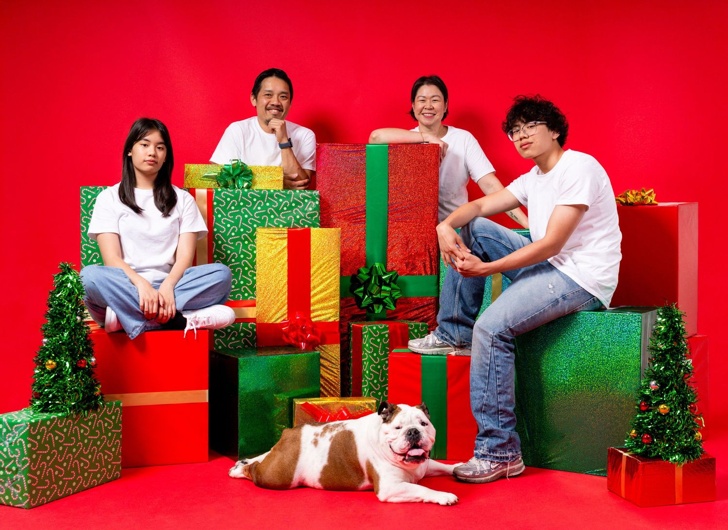 Four people and a bulldog pose with colorful Christmas gifts against a festive red background.
