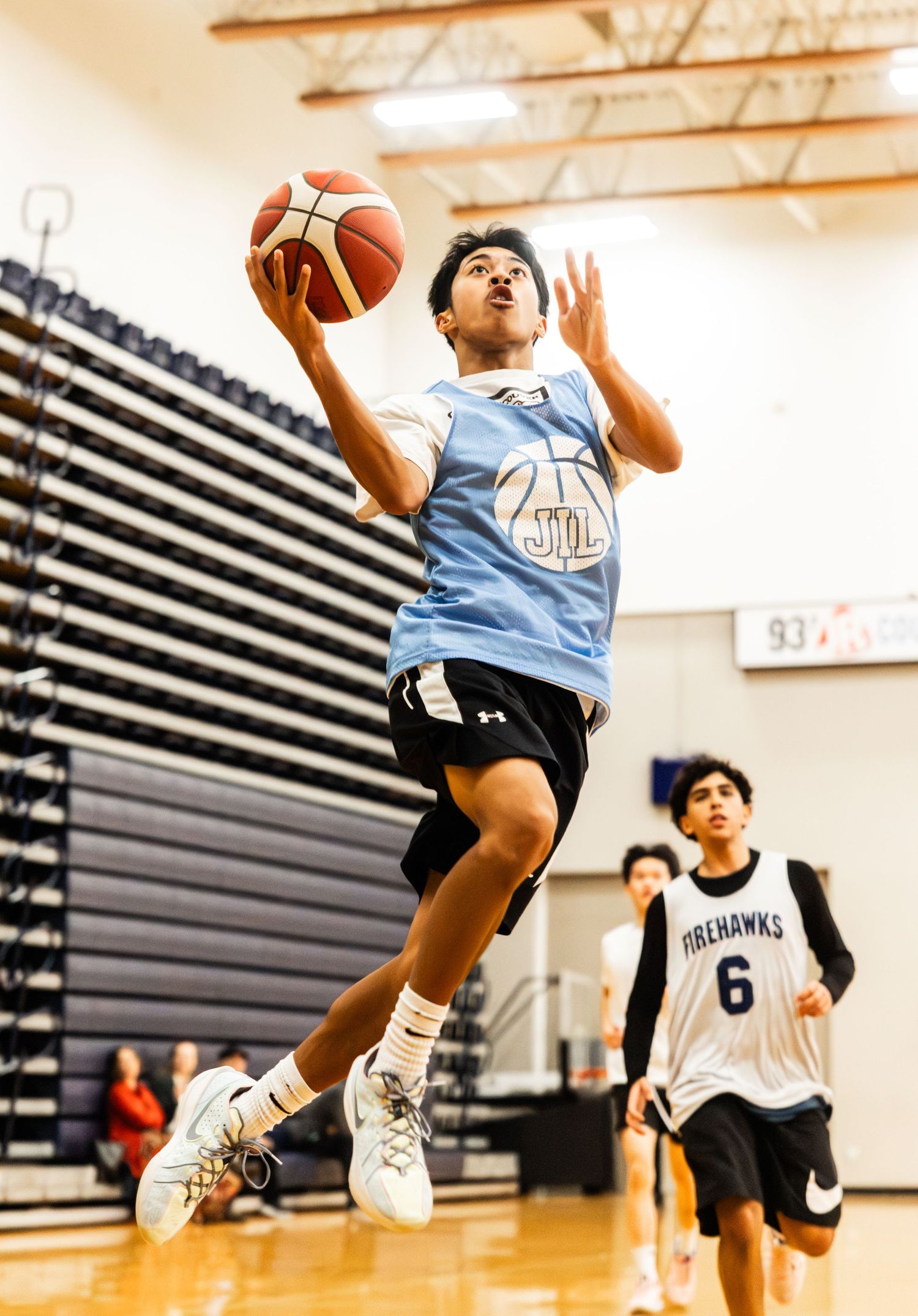 Young basketball player in blue jersey leaping for a layup during an indoor gymnasium game.