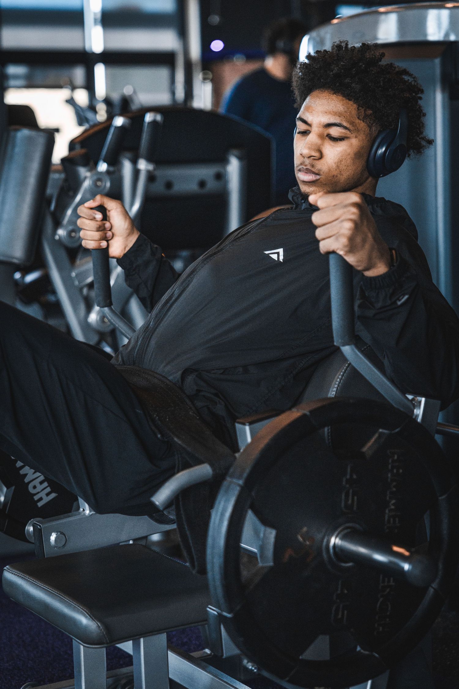 Young man in black gym wear and headphones working out on a chest press machine in a modern gym.