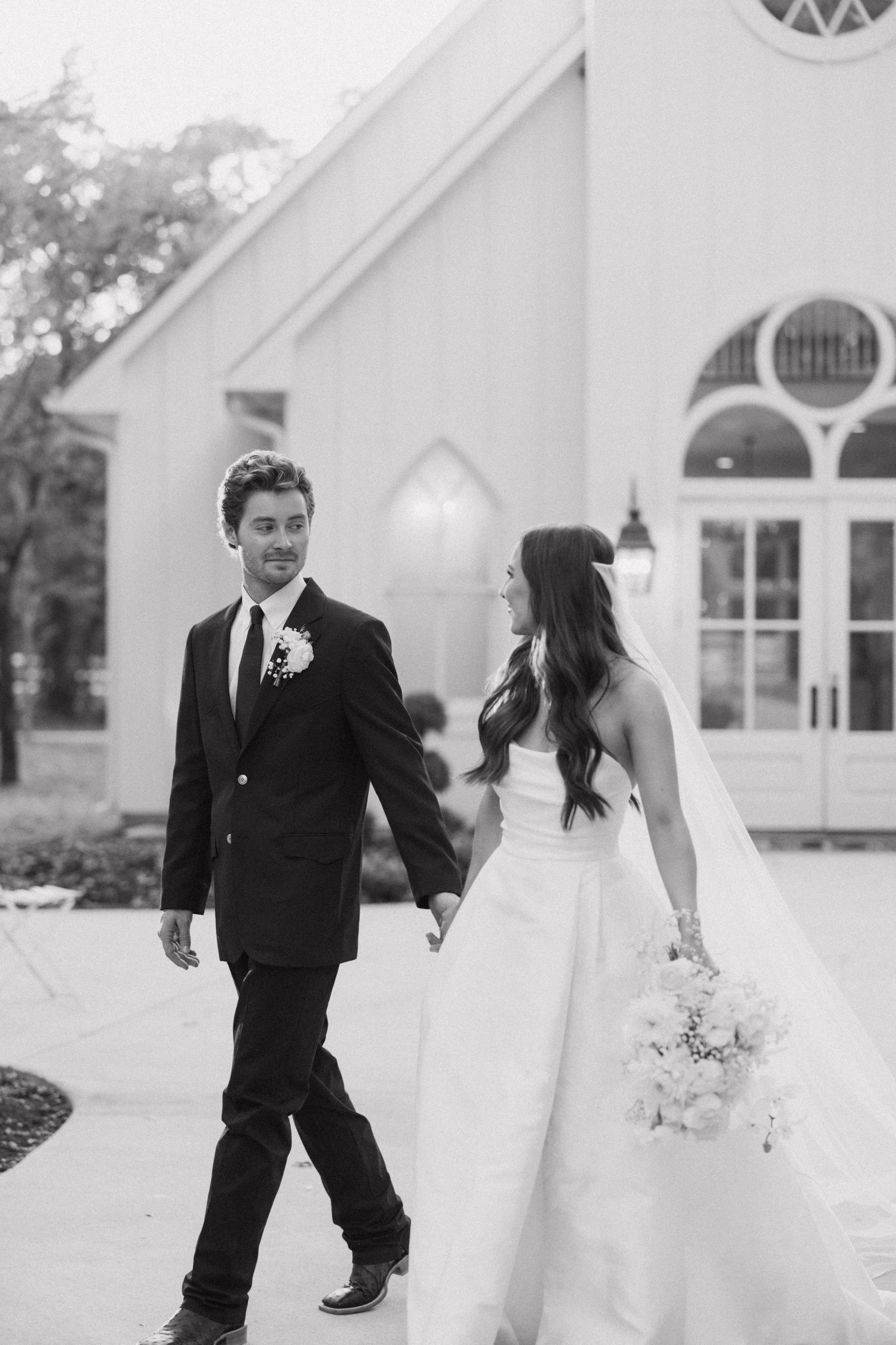 A playful moment between a bride and young ring bearer in formal attire outside a white church building.