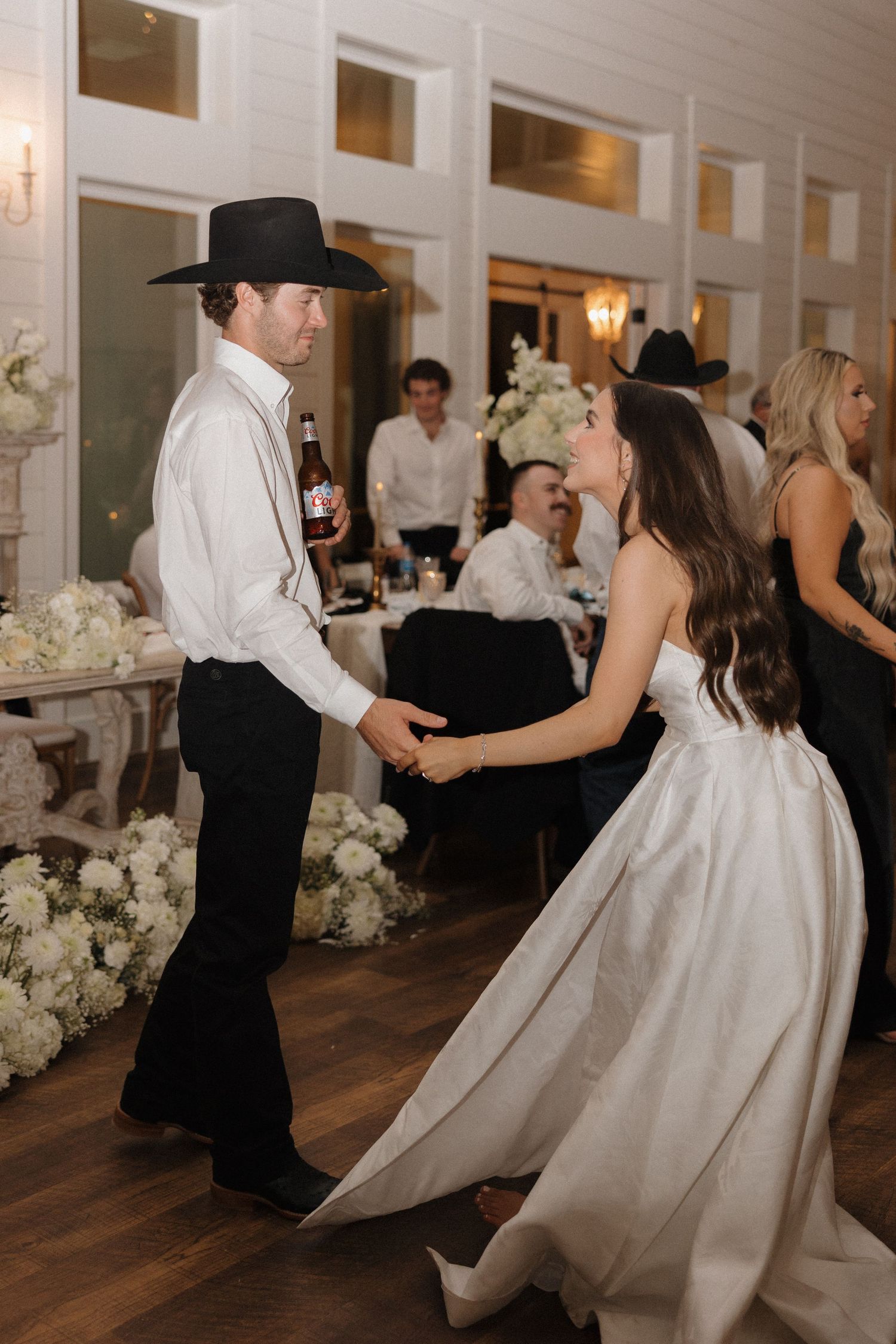 Dancers twirl across a wooden dance floor at an elegant reception decorated with white floral arrangements.