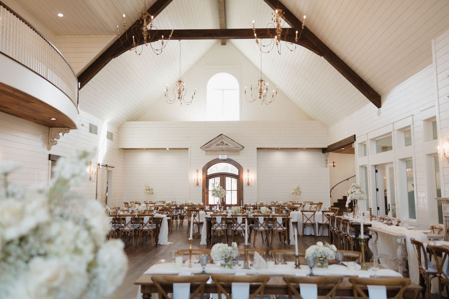 A bright and airy wedding reception venue with exposed wooden beams, white walls, and elegant chandeliers.