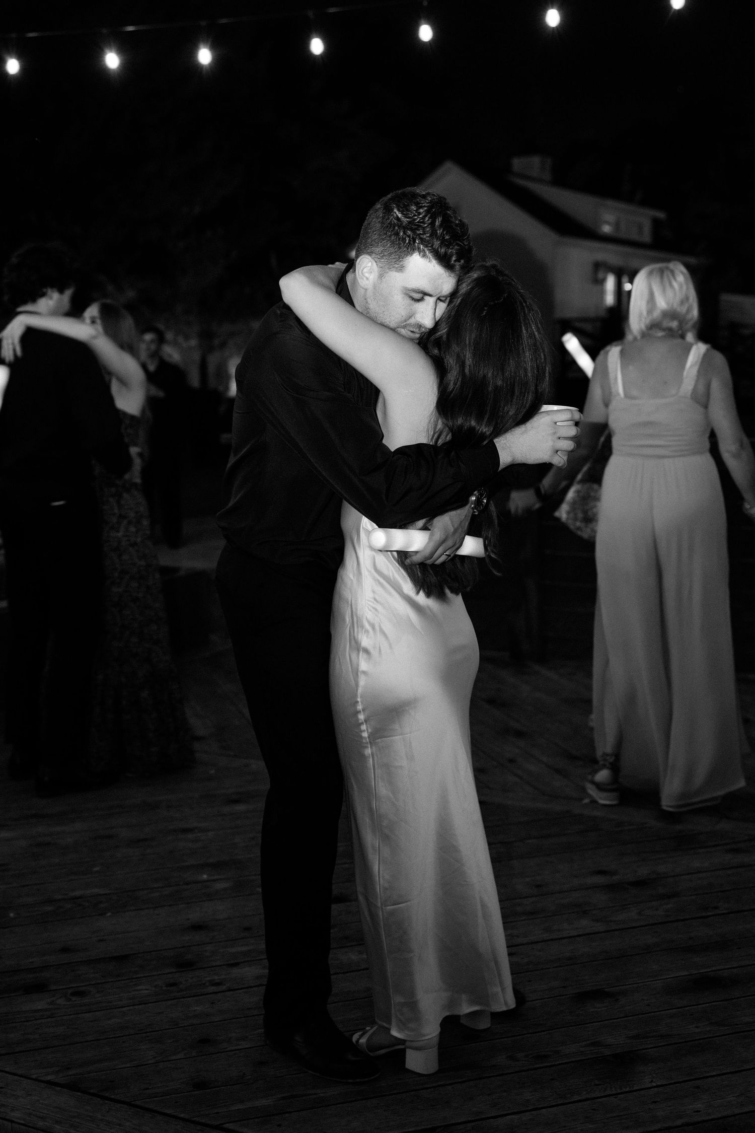 Couples dancing at a formal event on a dark dance floor under string lights.