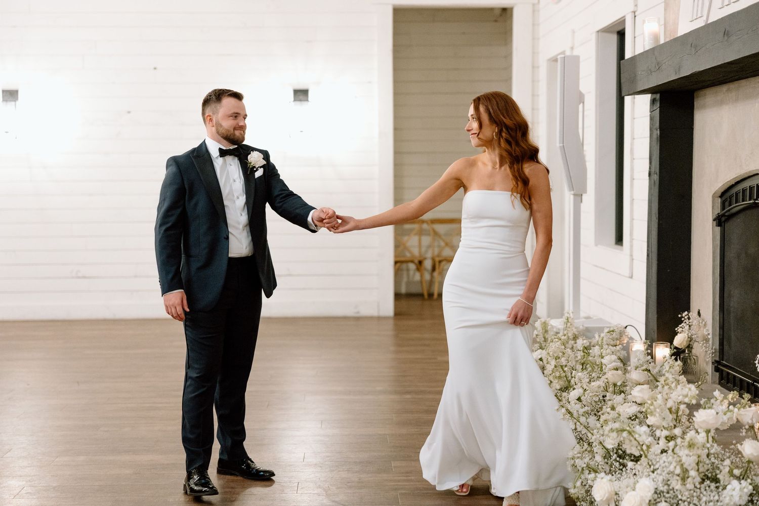 A romantic wedding first look moment captured in a bright indoor venue with white flowers and decor.