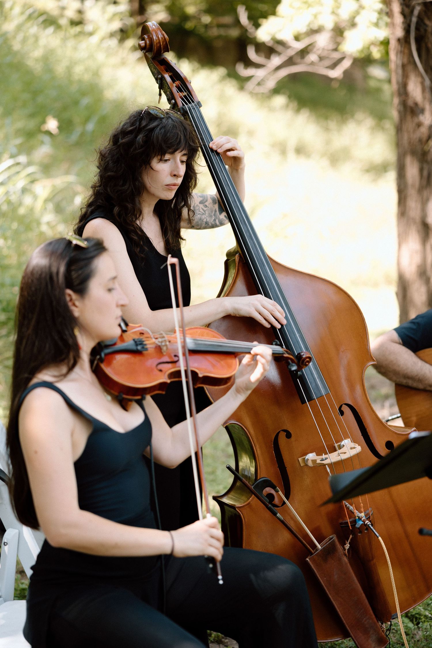 Musicians in black dresses perform with violin and upright bass during an outdoor classical music concert.