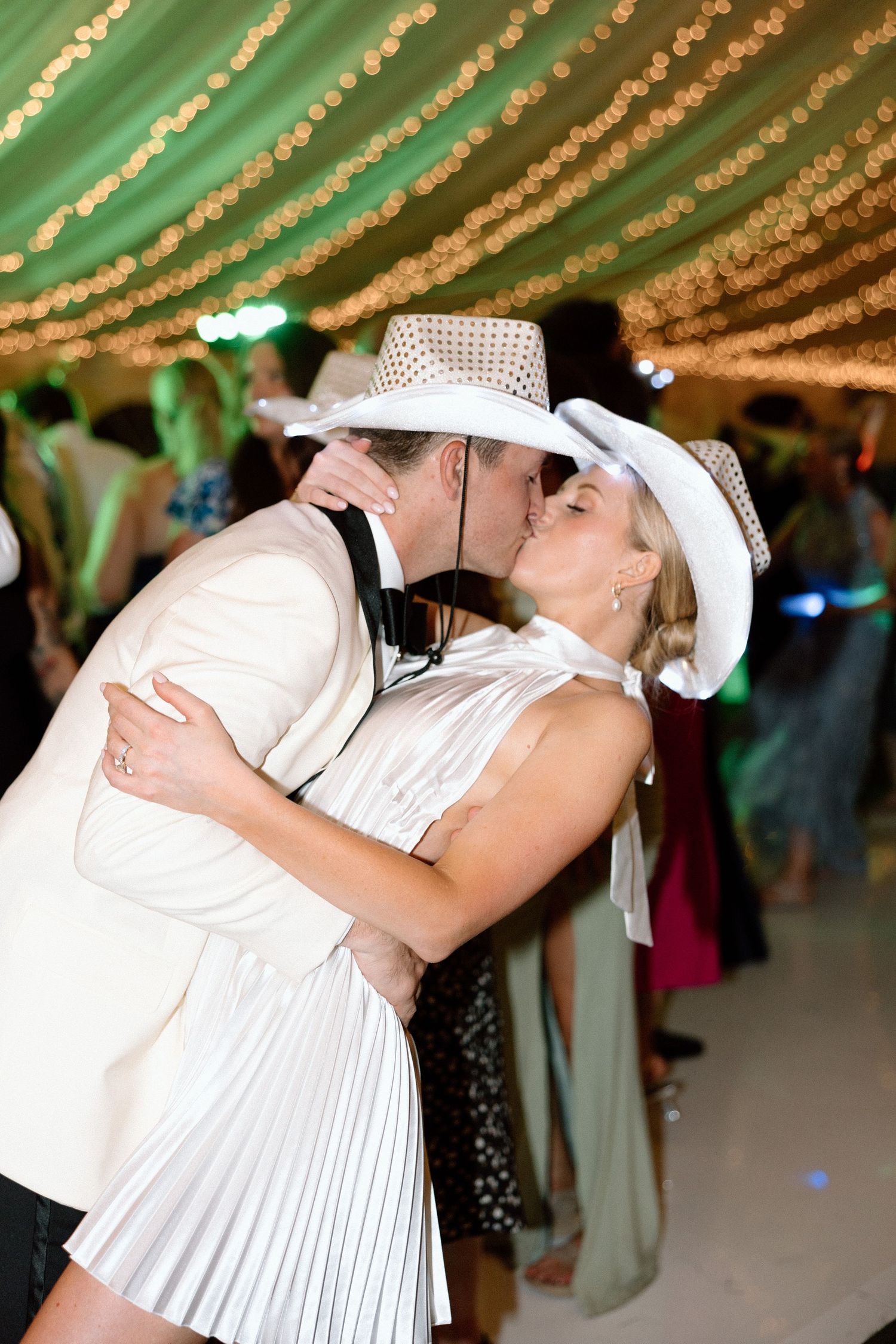 A romantic first dance at a wedding reception under twinkling string lights and green drapery.