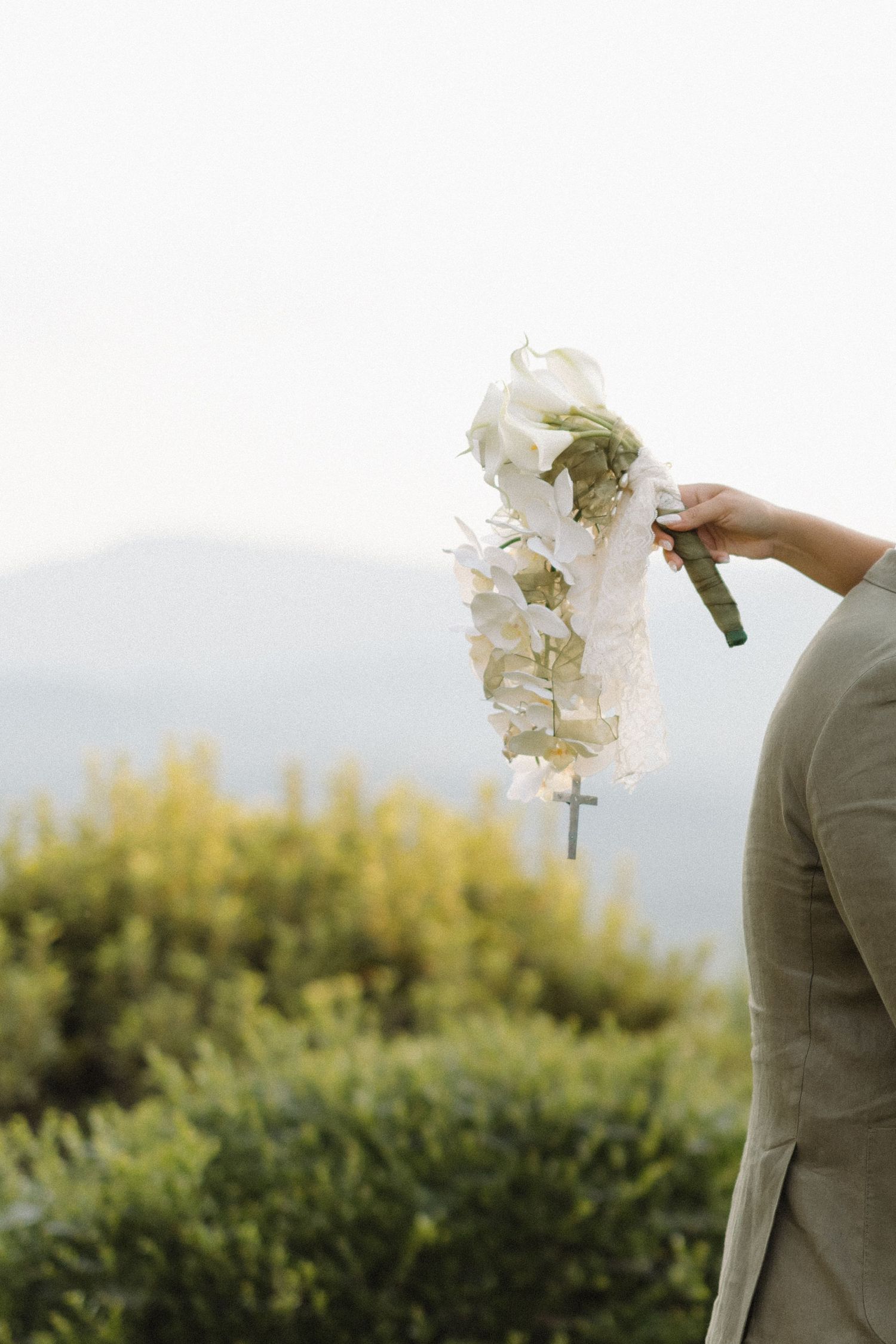 White orchid bouquet held against mountain landscape at sunset.