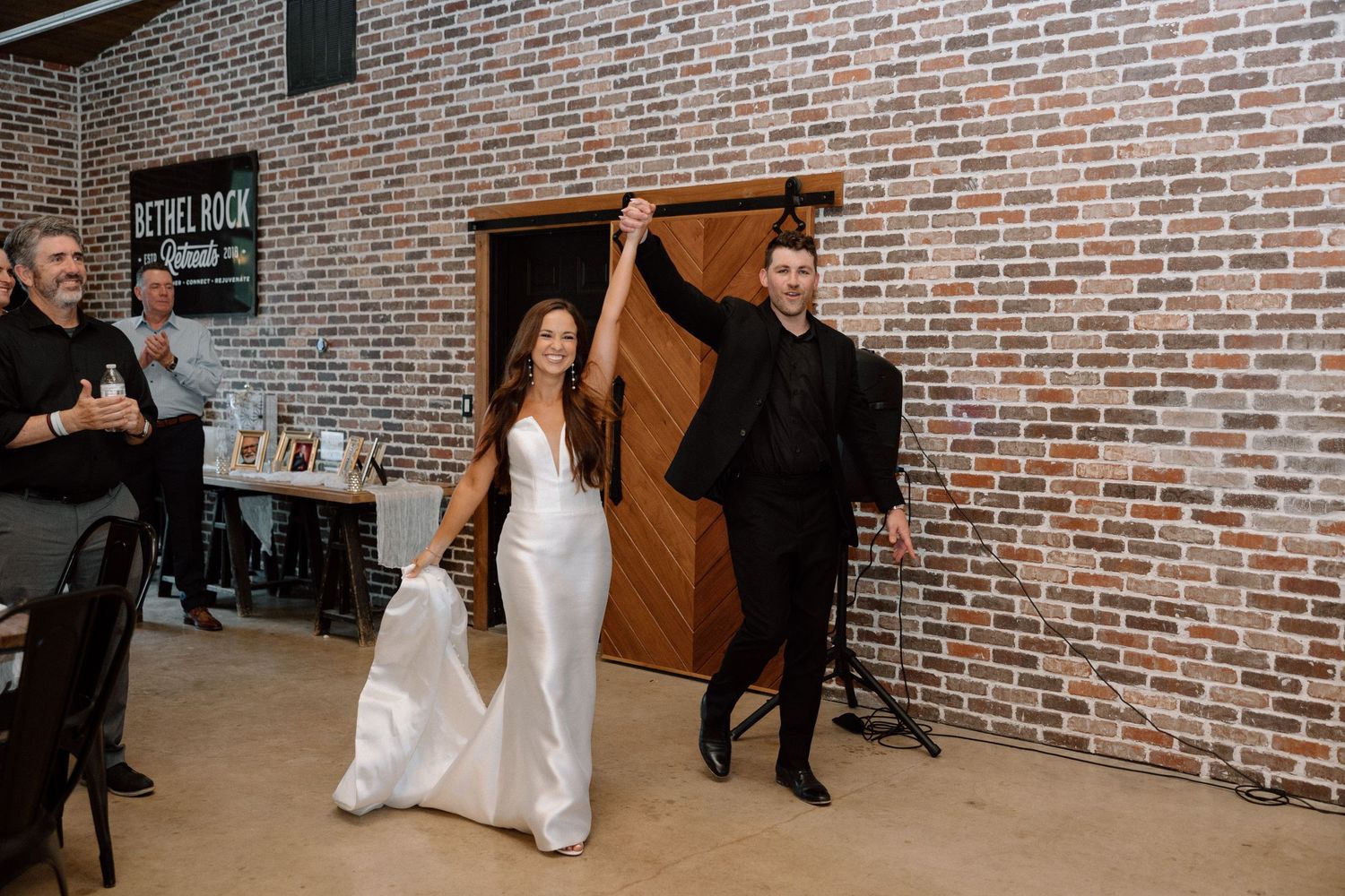 A group of dancers perform in a rustic brick-walled venue during a wedding celebration.