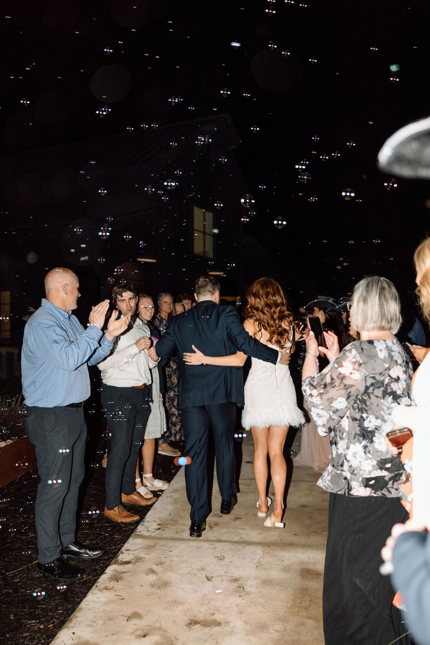 People dancing in a line at a wedding reception or party with dark lighting and a light-colored floor.